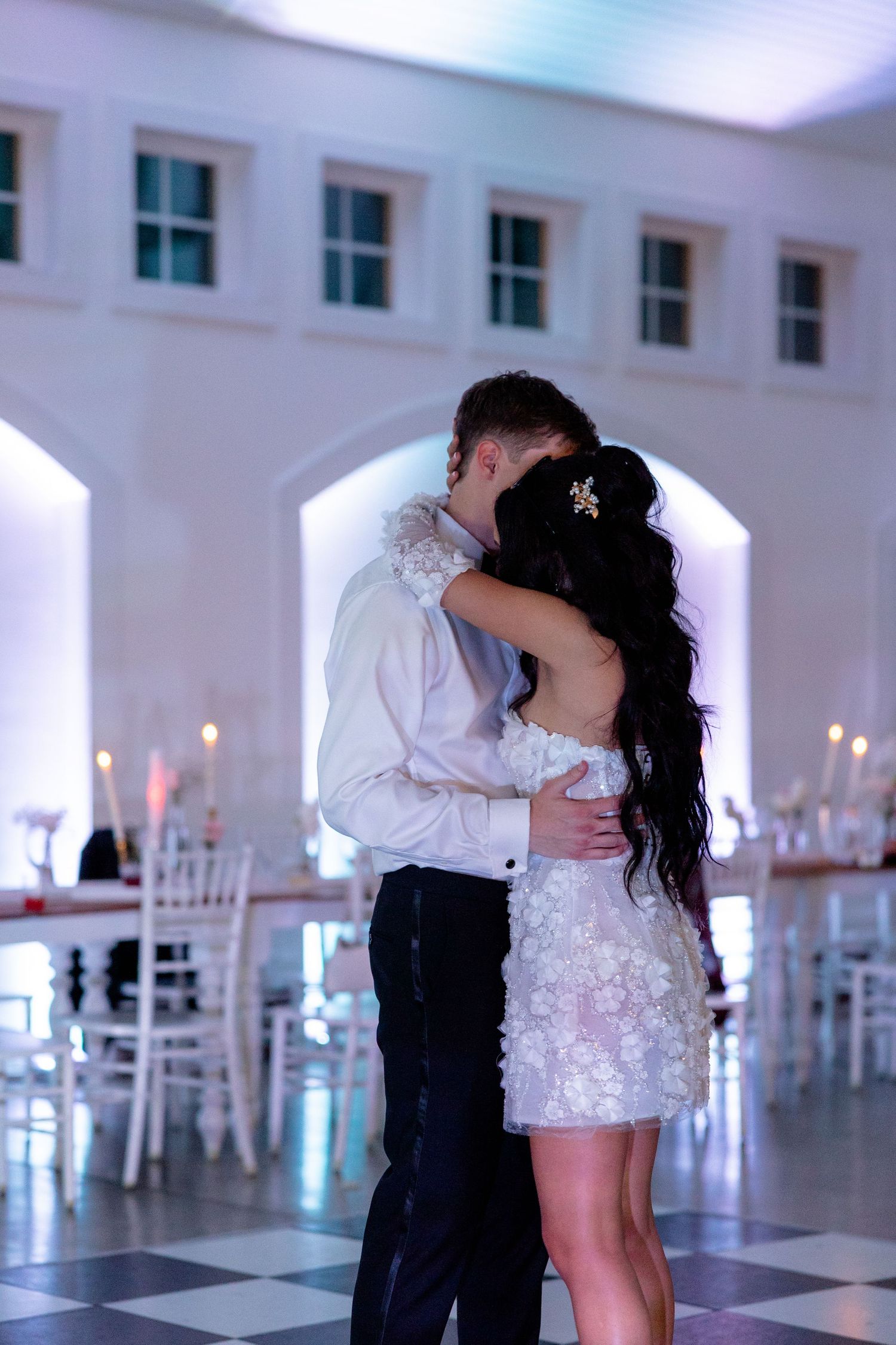 Romantic dance in an elegant white reception venue with checkered floors and white chairs.