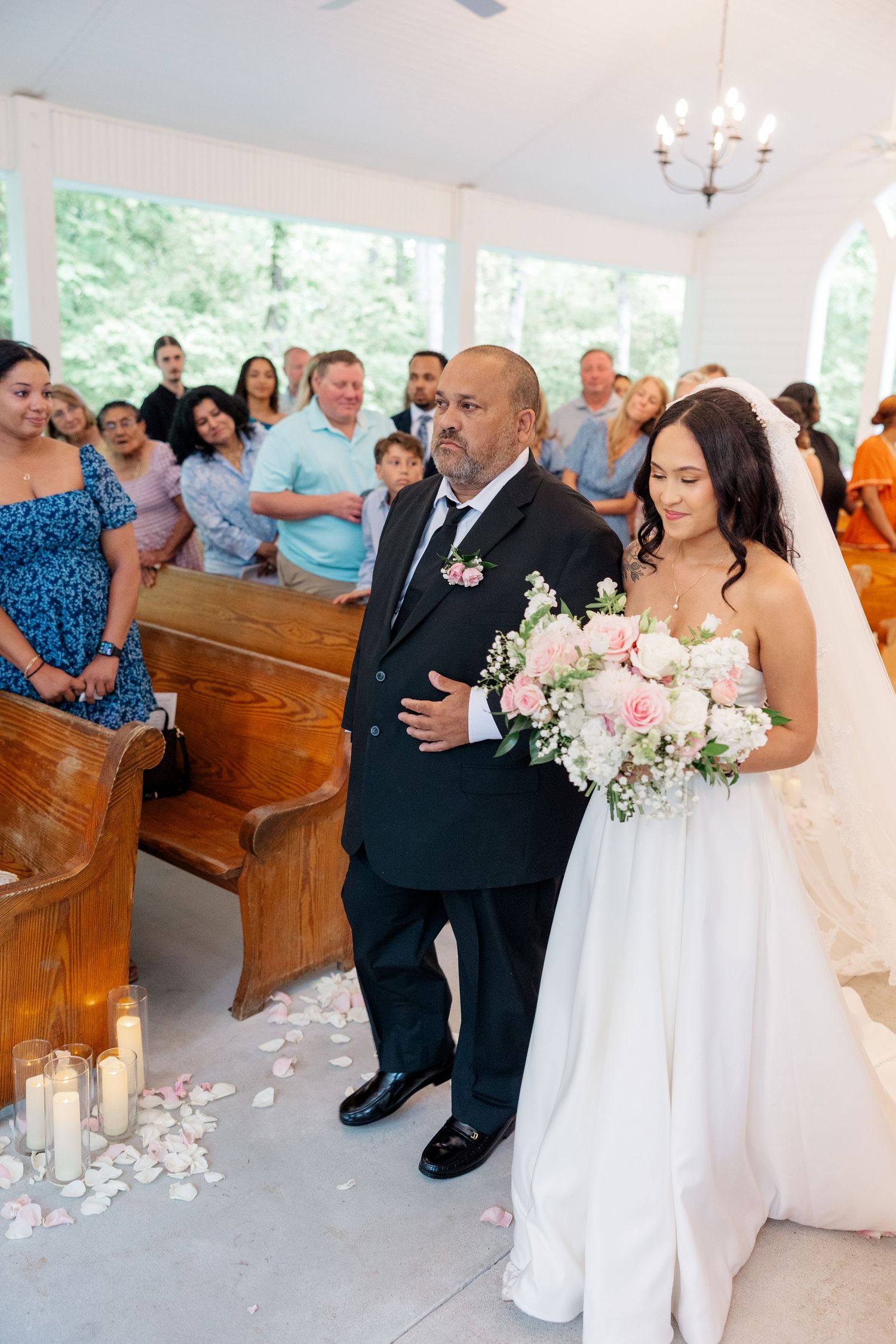 Wedding ceremony inside white chapel with wooden pews and floral decorations.