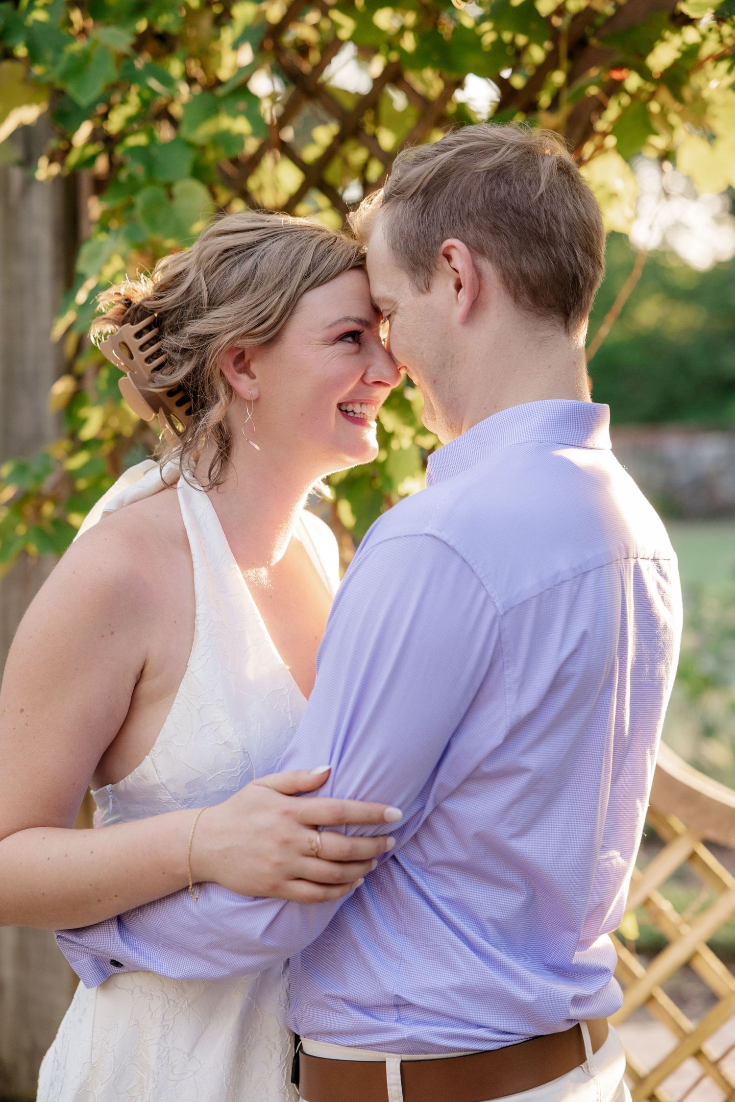 A couple shares an intimate moment in golden sunlight beneath trees during an outdoor photoshoot.