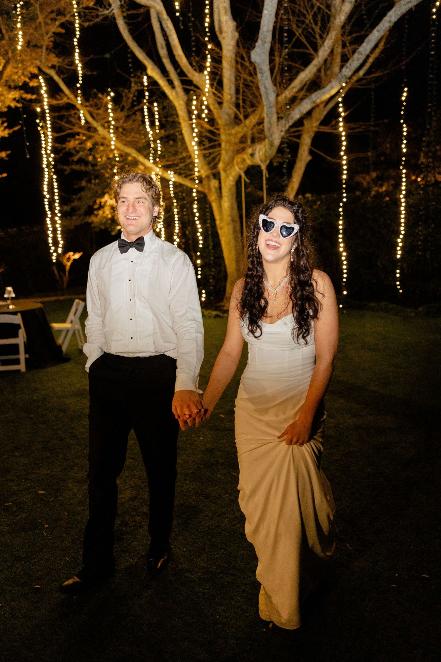 Couple enjoying nighttime wedding reception under trees decorated with twinkling string lights.