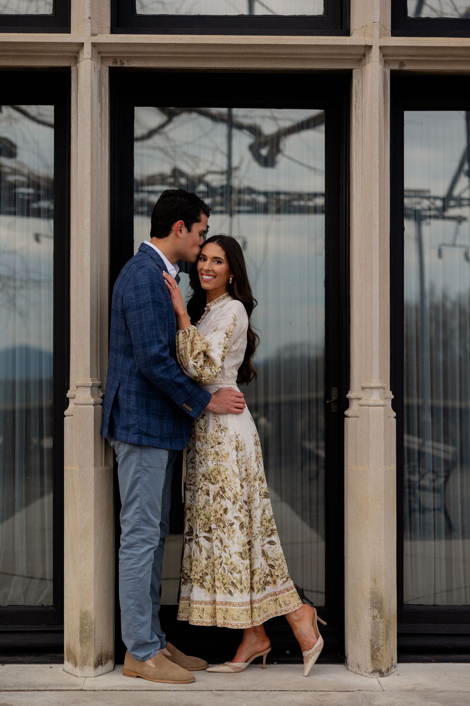 A couple in classic and traditional ethnic attire share an intimate moment between architectural columns at sunset.