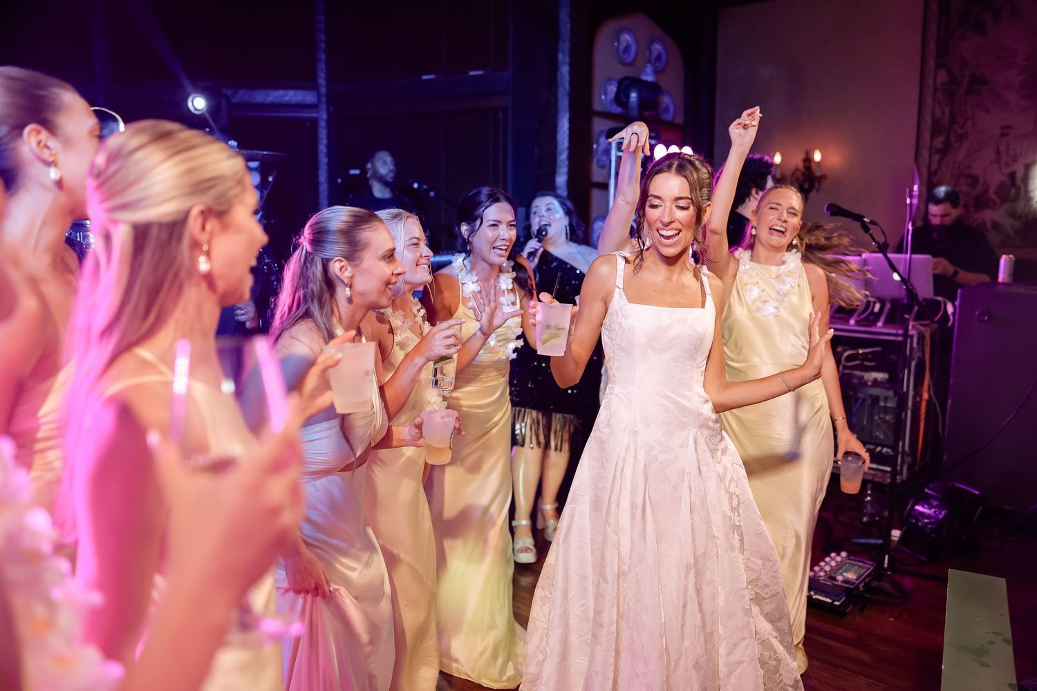 Bride in white gown dancing joyfully with bridesmaids in gold dresses at a wedding reception.