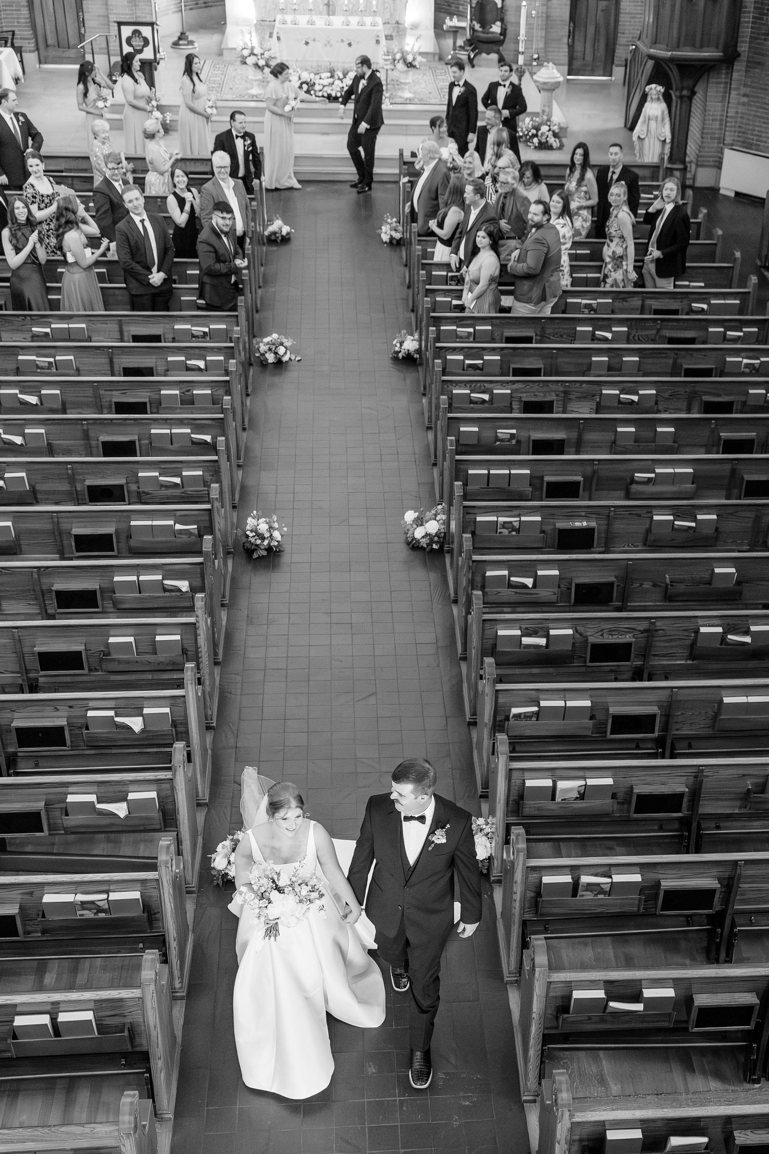 Aerial black and white photo of bride and groom walking down the aisle after their church wedding ceremony.