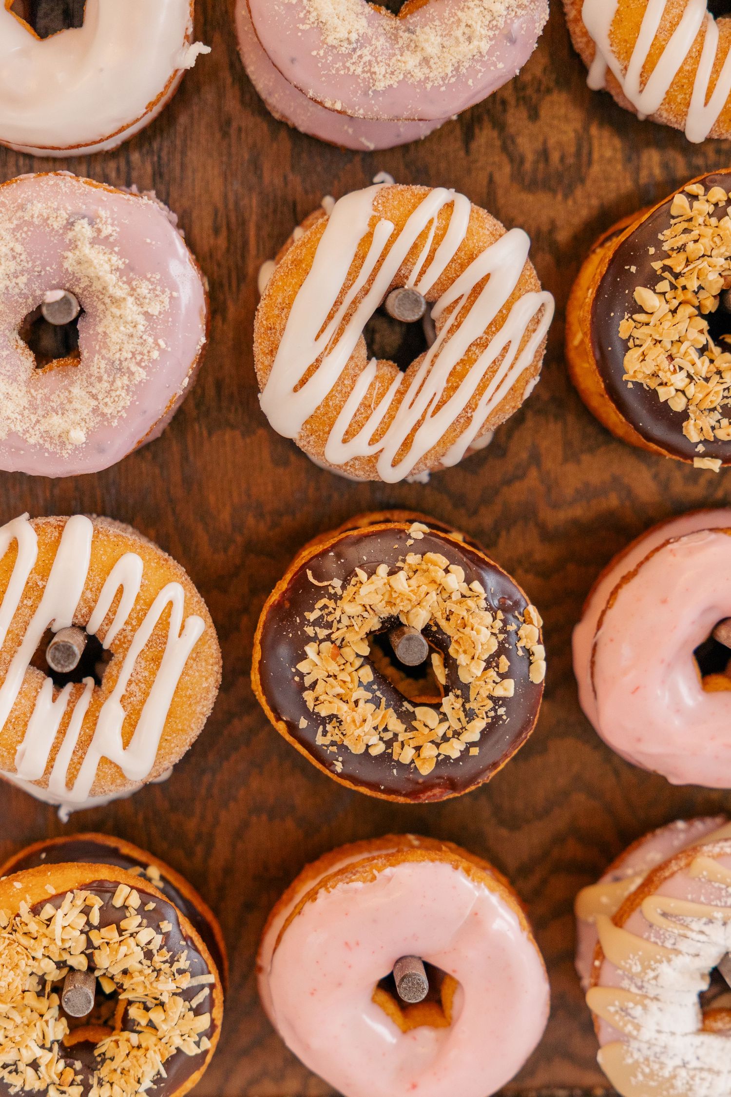 Assorted decorated donuts with pink, chocolate, and white glazes on wooden surface for wedding dessert.