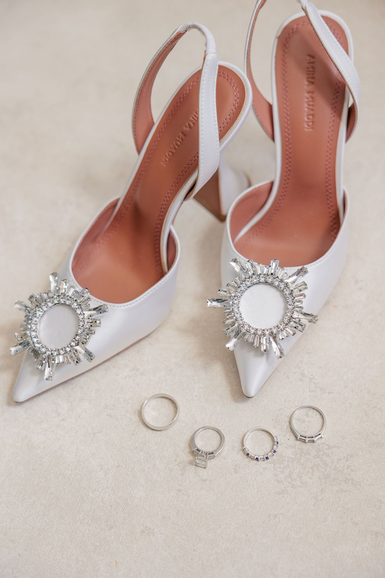 White slingback wedding heels with crystal sunburst brooch displayed alongside diamond wedding rings.