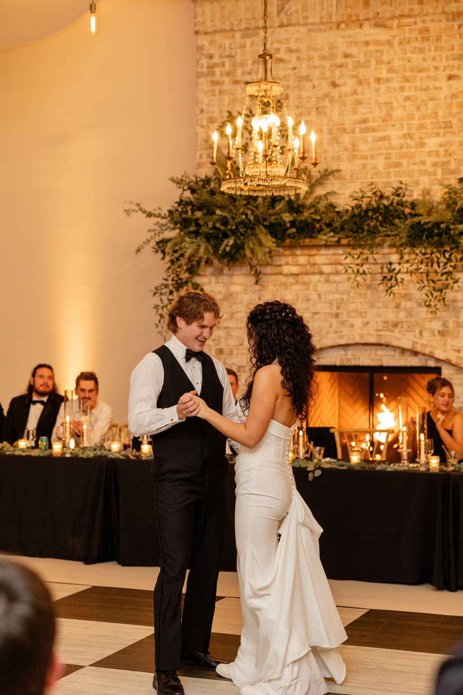 A romantic first dance in an elegant reception venue with brick walls and a crystal chandelier.