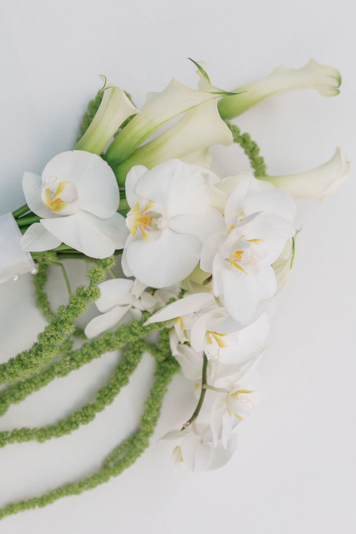 Delicate white orchids with green foliage arranged in a minimalist composition against a light background.
