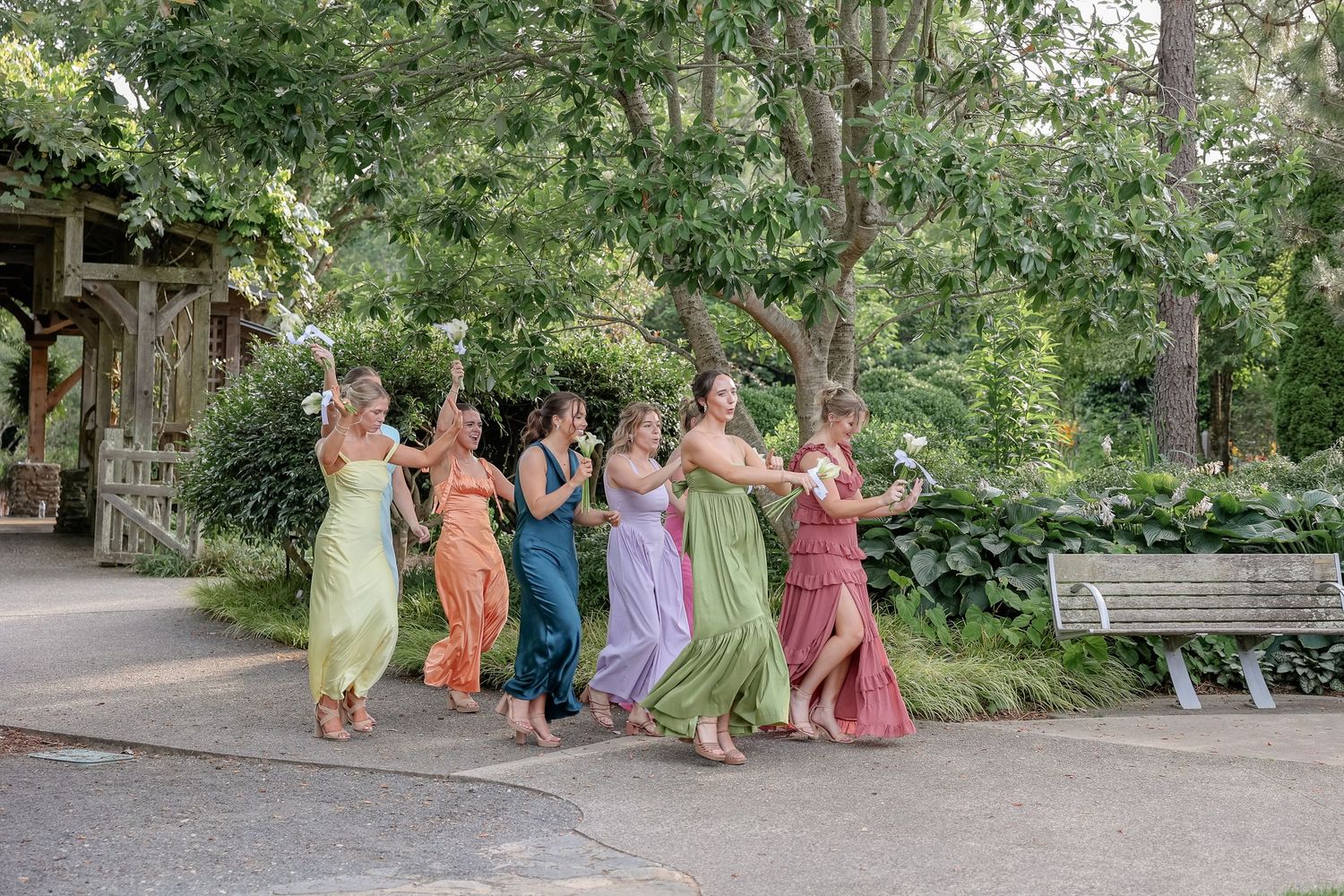 Bridesmaids in pastel dresses pose playfully outdoors during wedding celebrations.