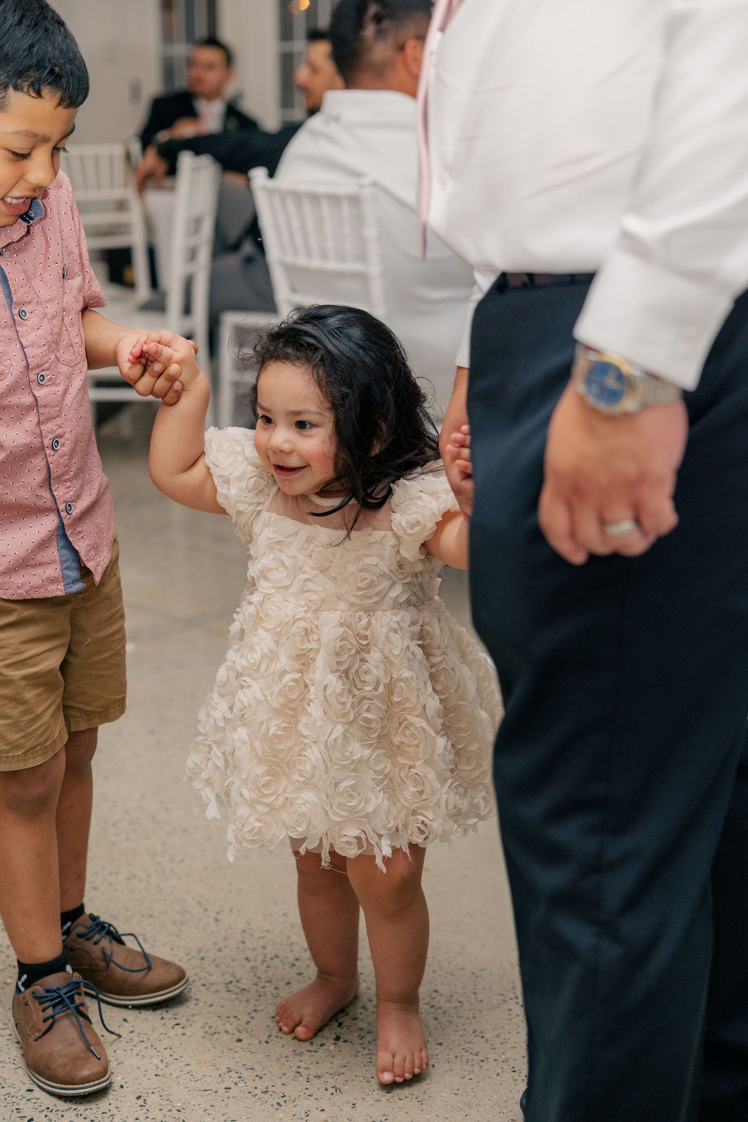 Children and adults stand on a polished concrete floor during a party event with festive dress attire.