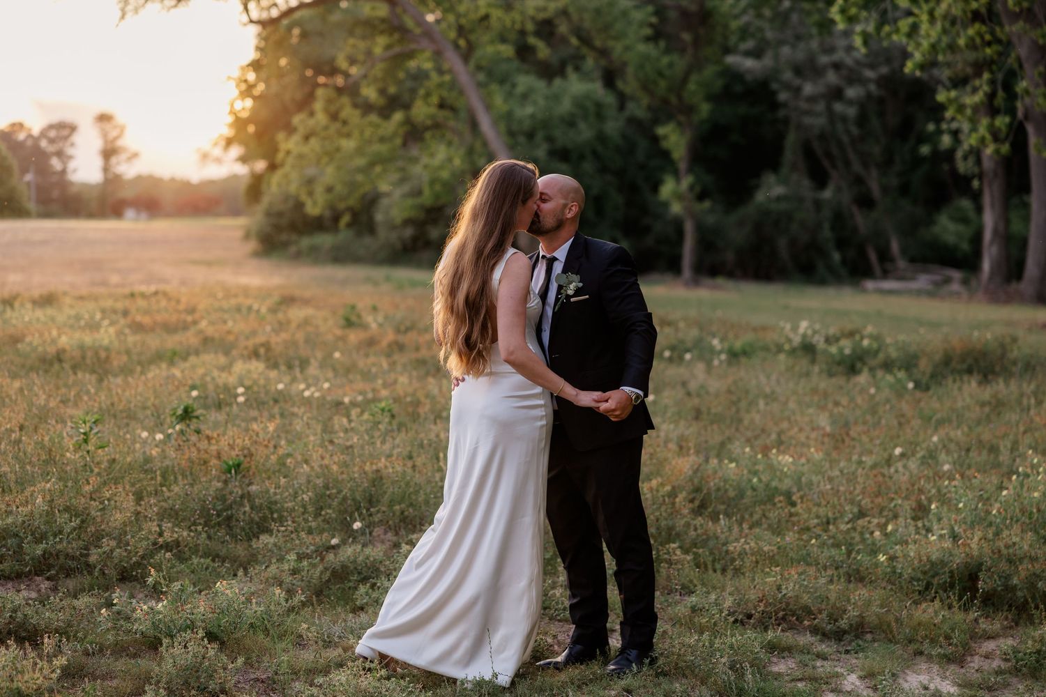 Couple takes romantic sunset photos in a golden-lit field during their wedding day.