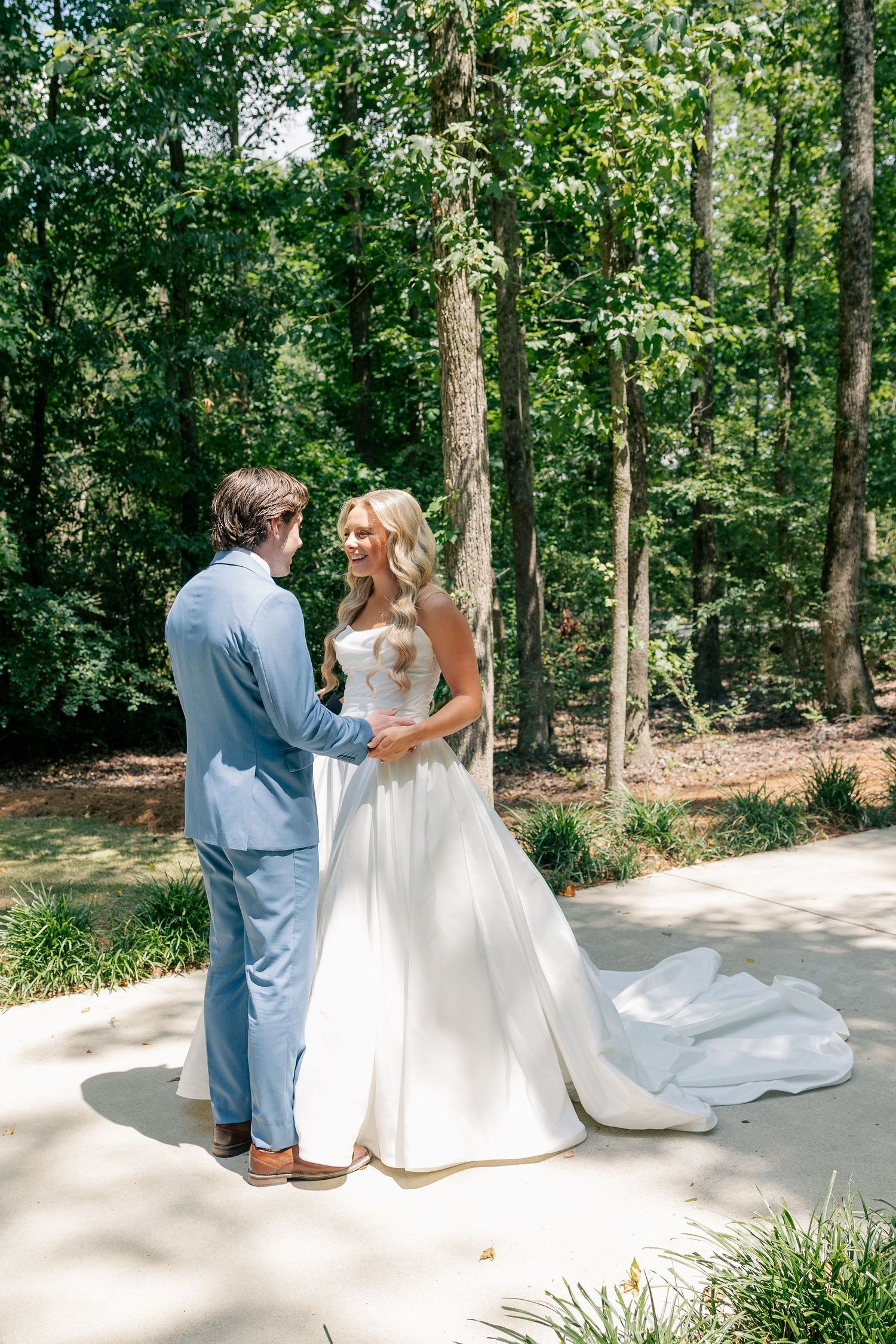 Bride and groom share a first look moment outdoors surrounded by lush green trees.