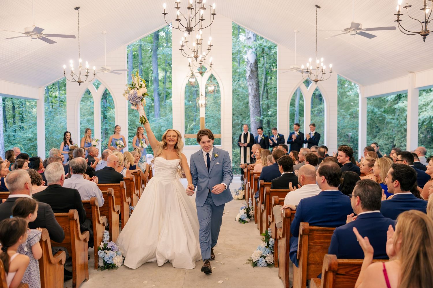 Bride and groom joyfully walk back down the aisle after their ceremony in a stunning white chapel.