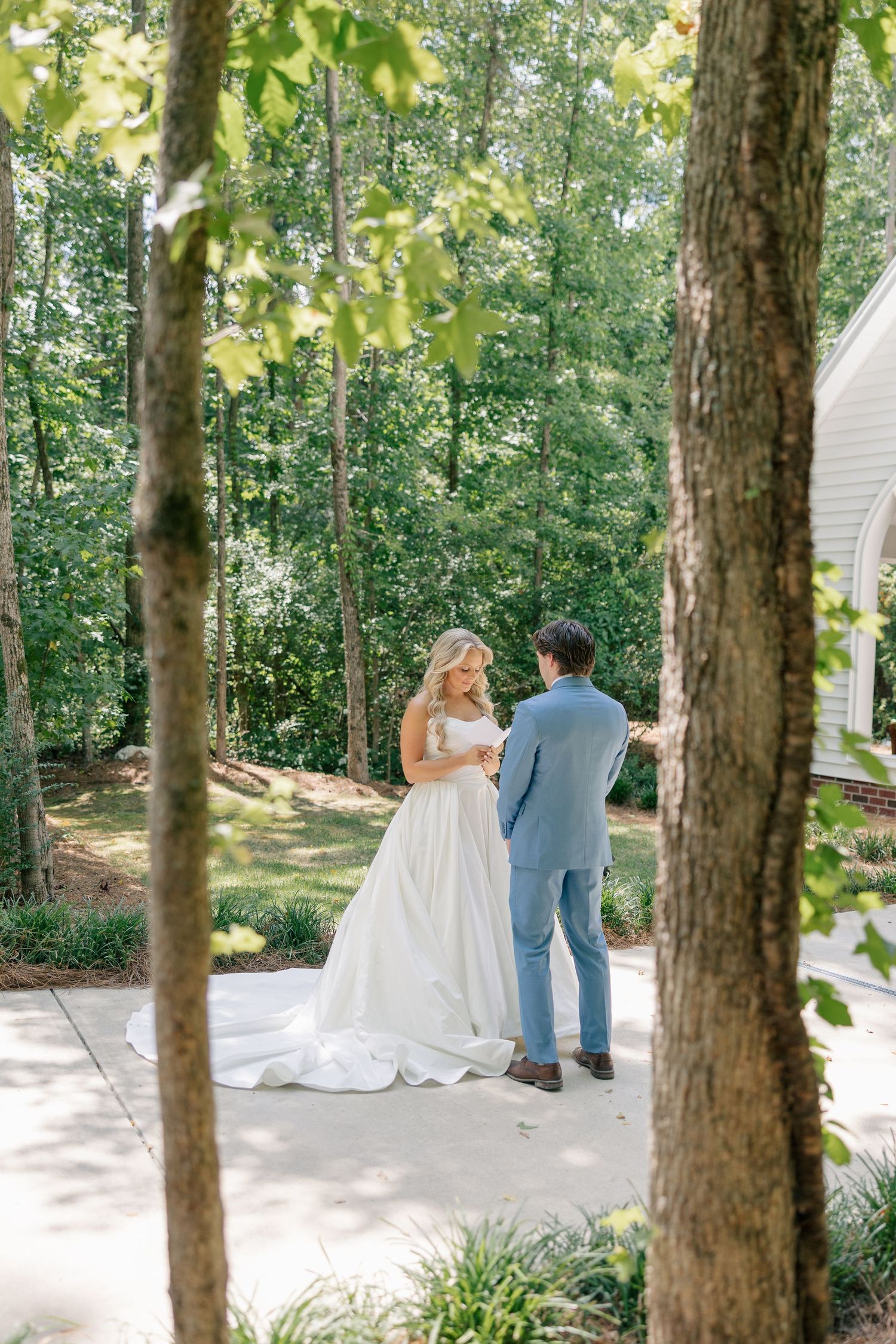 Bride and groom share first look moment among lush green trees outdoors.
