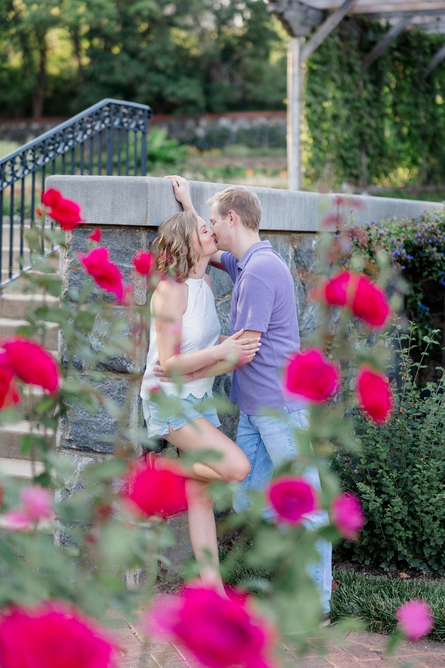 A romantic couple embraces among vibrant pink flowers in a garden setting during a photo session.