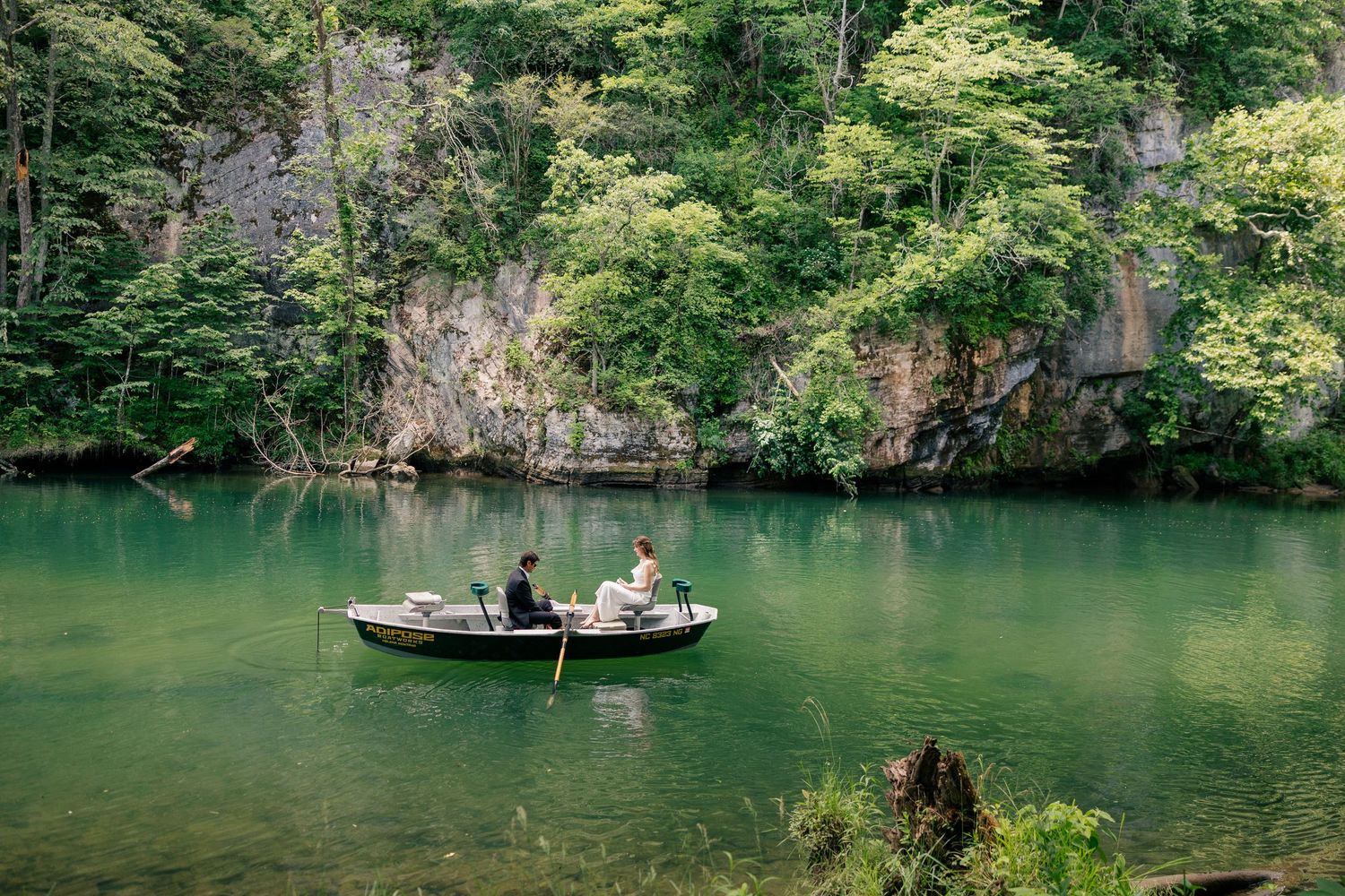 Bride and groom rowing a small boat on a tranquil emerald green quarry lake.