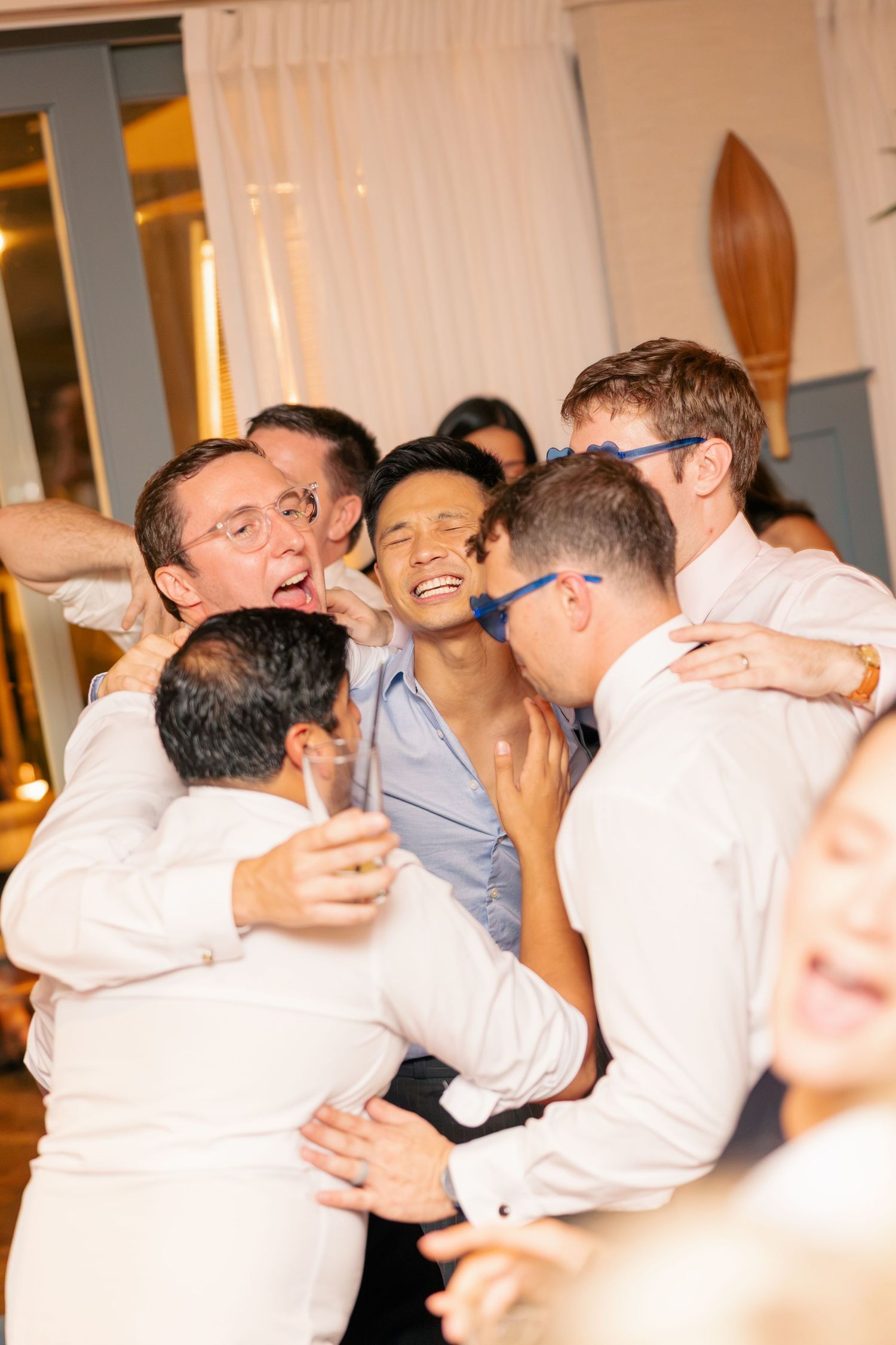Wedding guests joyfully hugging and celebrating together on the dance floor at reception.