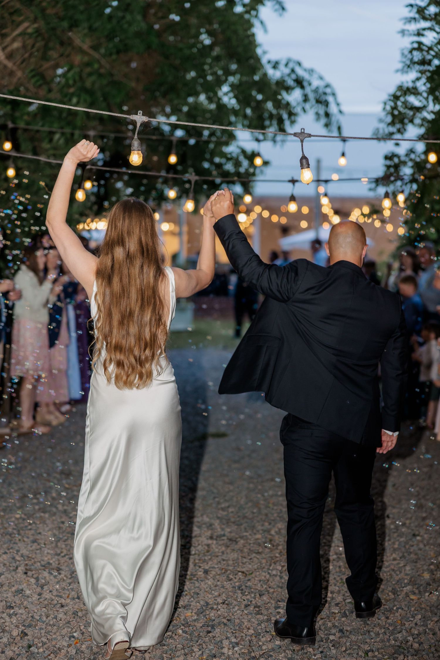 Joyful couple dancing at outdoor wedding reception under twinkling lights.
