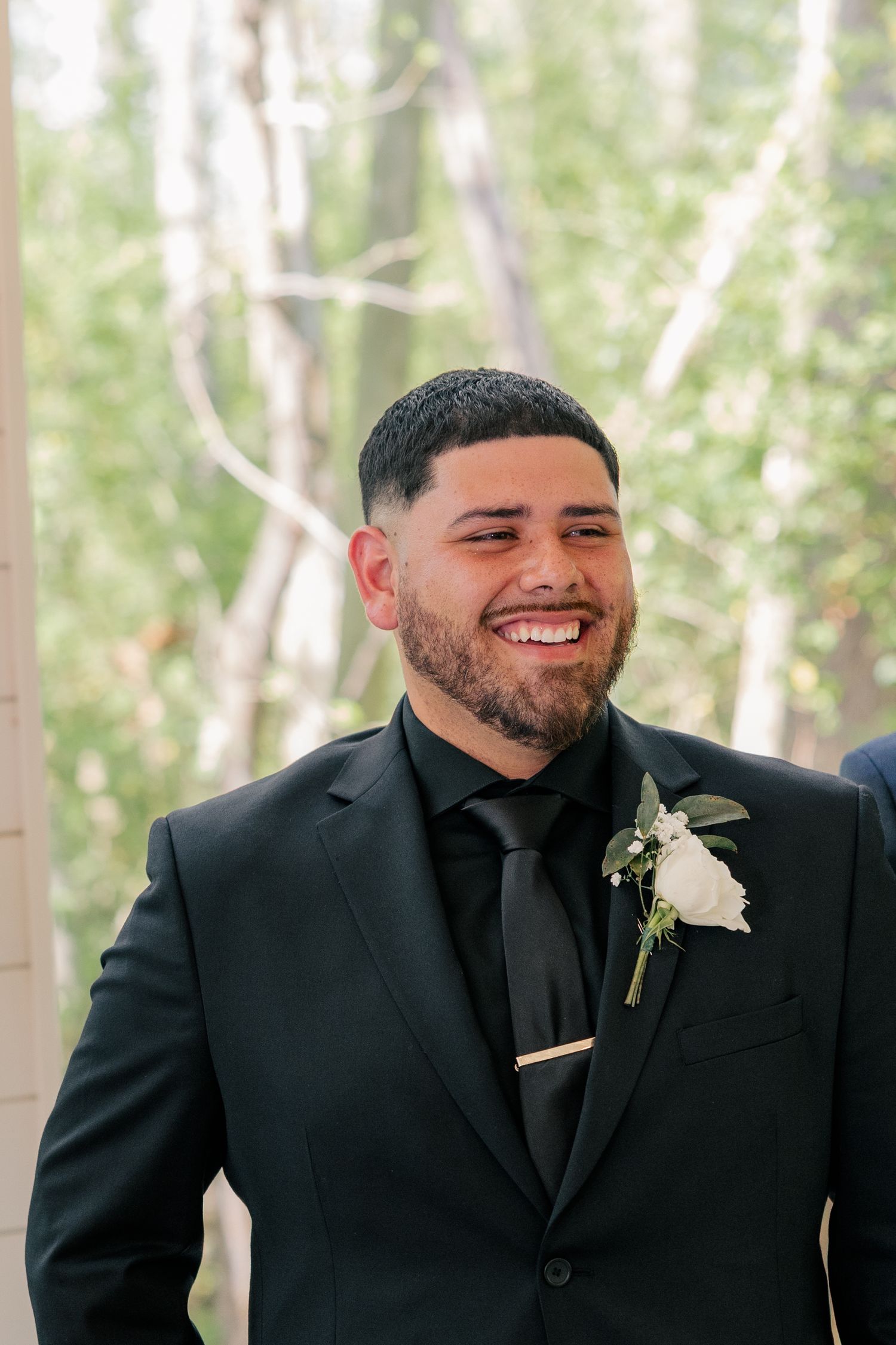 Wedding party members in black suits with white boutonnieres share smiles during a celebration.