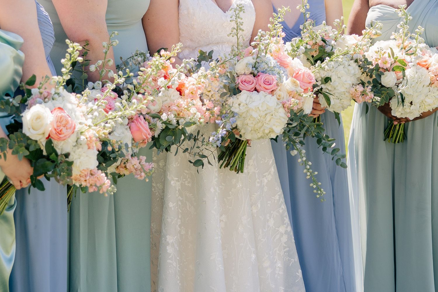 Row of coordinated floral bouquets in soft pink and white blooms with greenery against blue backdrop.