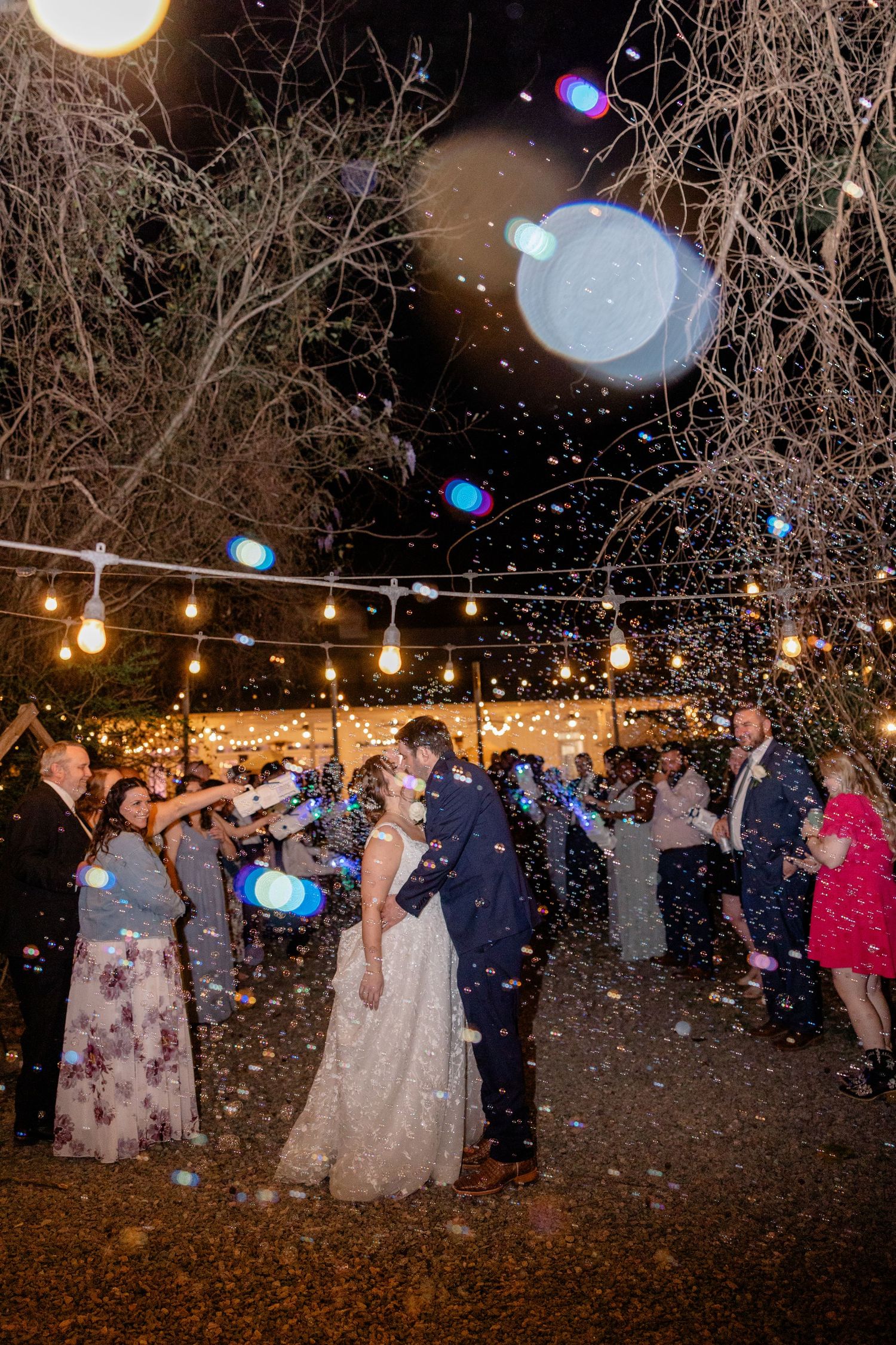 Outdoor nighttime wedding celebration with string lights and snowfall effects.