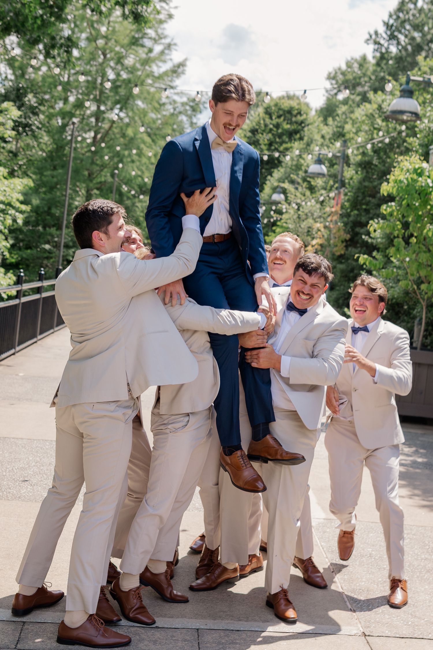 Groomsmen in tan suits and navy jackets posing playfully on outdoor steps.