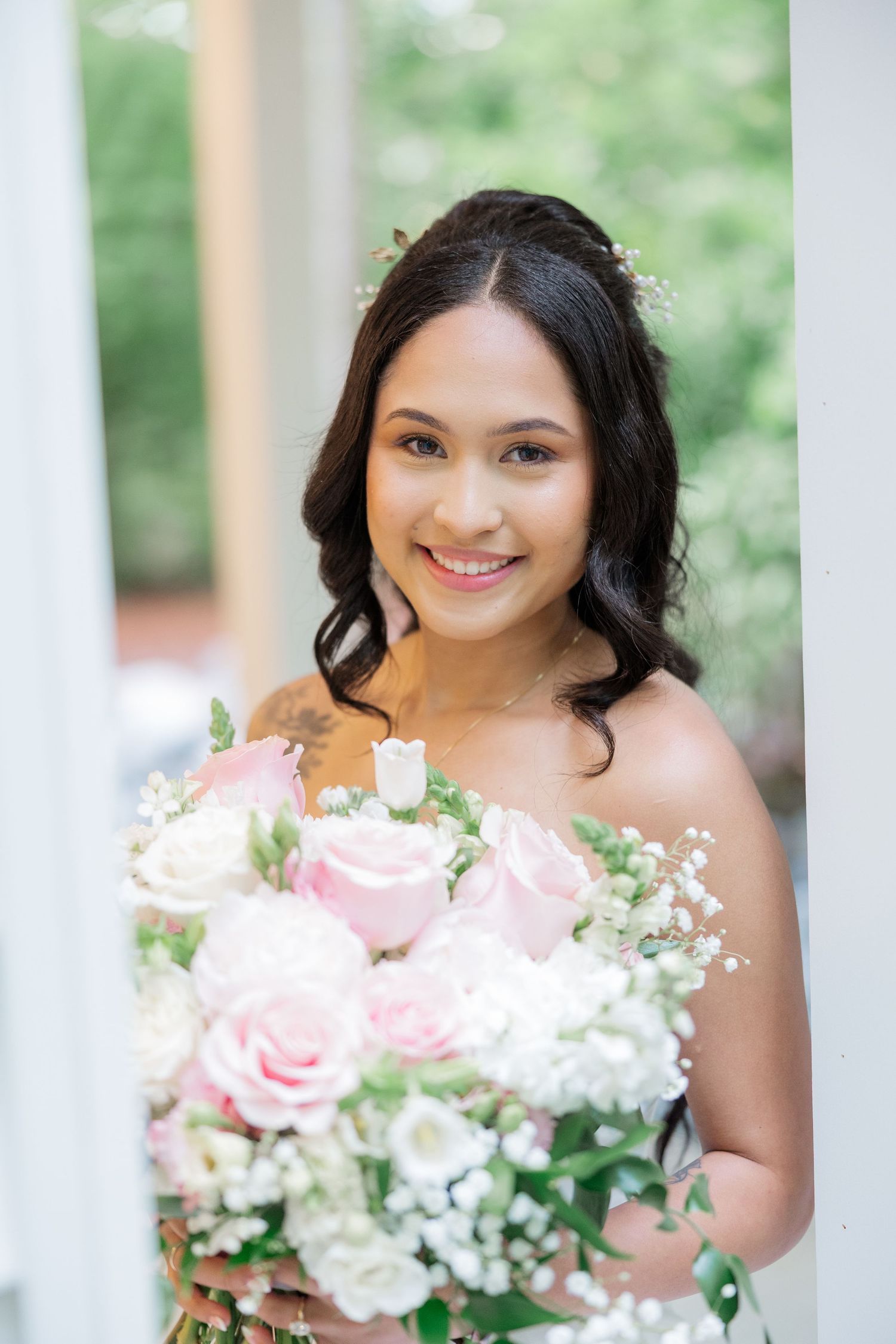 Bride holds a beautiful bouquet of pink and white roses with baby's breath against a bright outdoor backdrop.