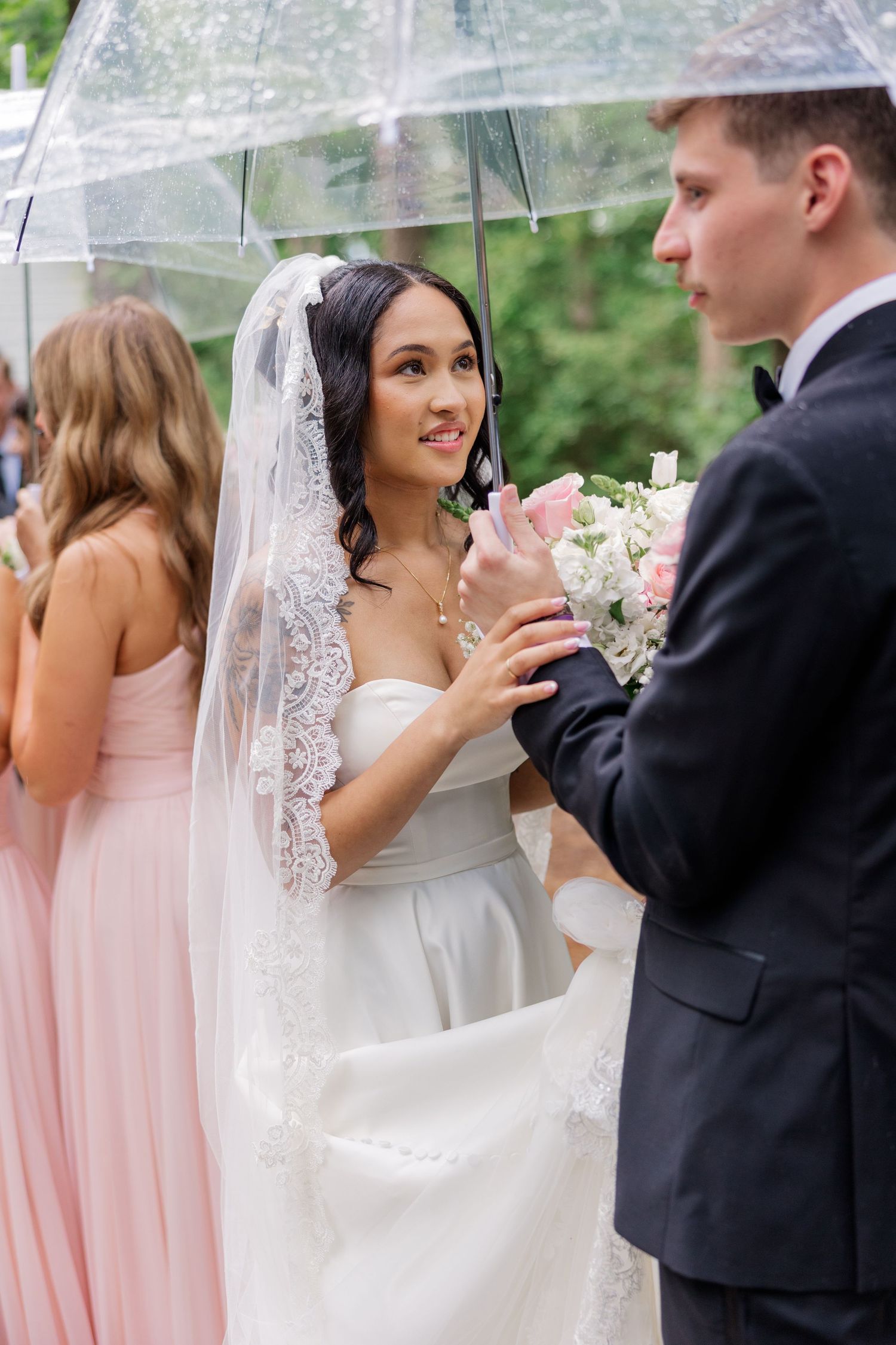 Wedding party poses under clear umbrellas with bridesmaids in pink dresses.