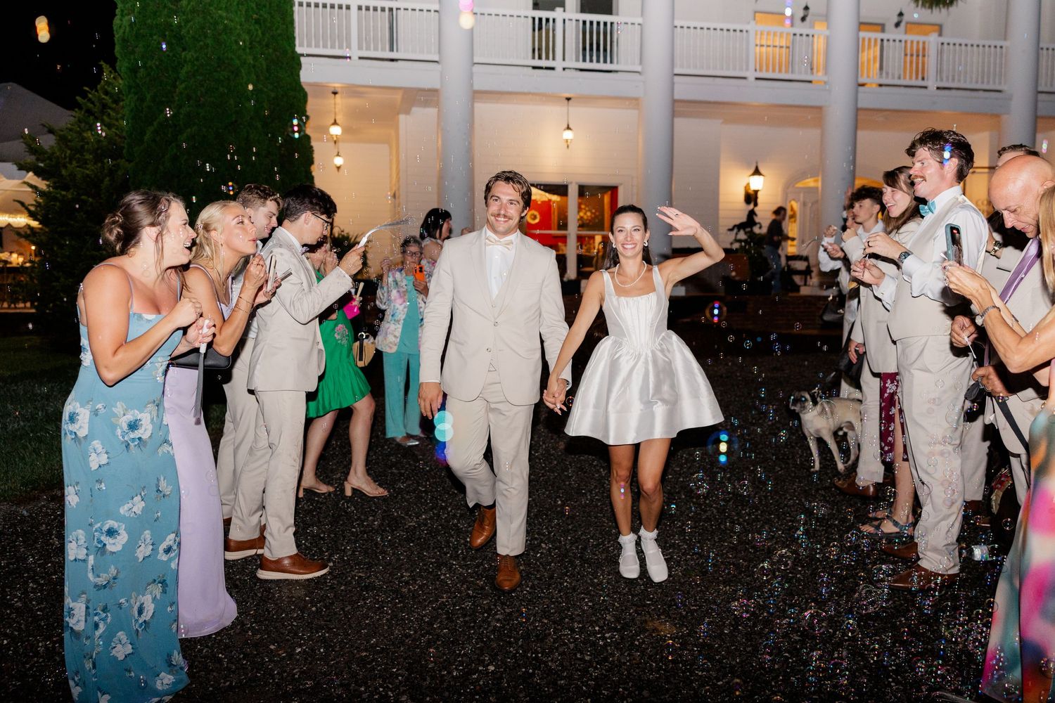 Wedding party and guests dancing and celebrating outdoors at night under string lights.