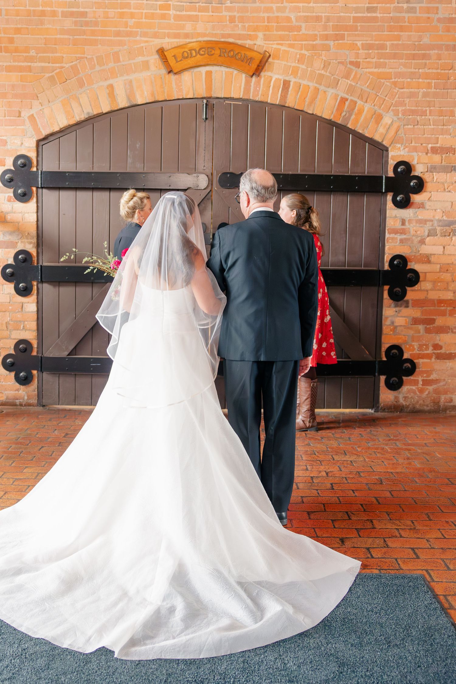 Bride in white gown with veil stands with groom before large wooden doors at wedding venue.