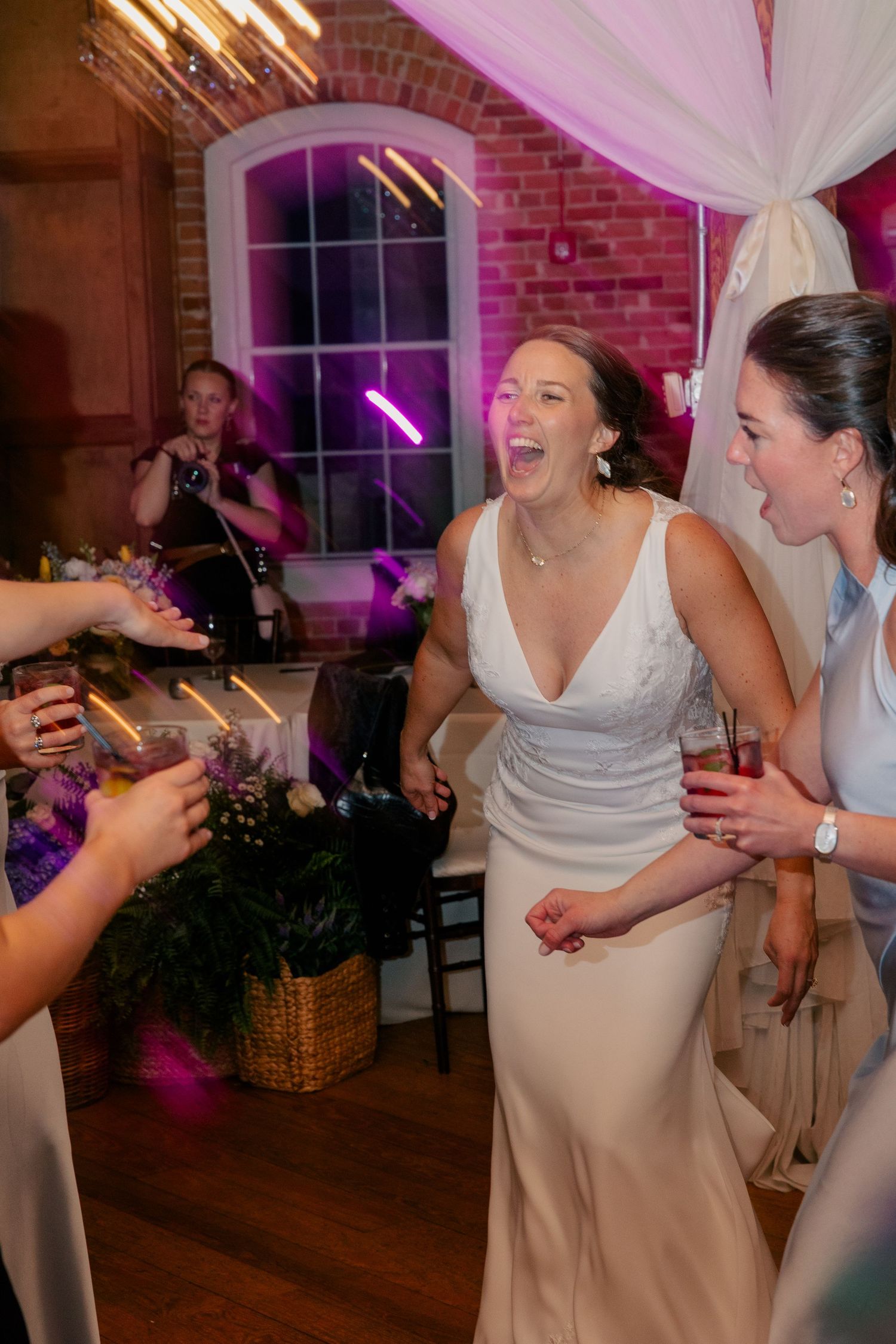 Joyful bride in white gown laughs with guests during lively wedding reception dance floor celebration.