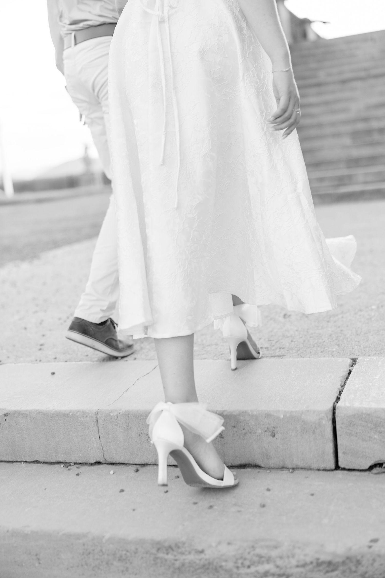 Close-up view of white wedding shoes walking on concrete in black and white photography.