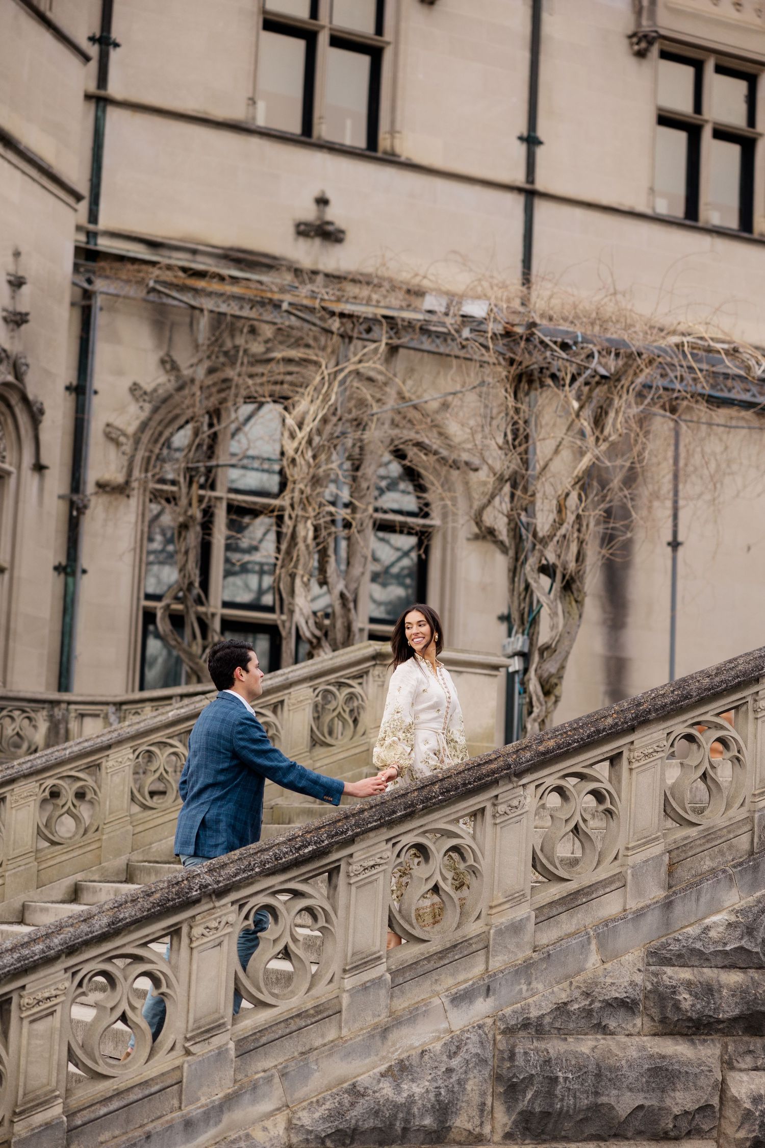 A couple shares a romantic moment on an ornate stone staircase with vintage architecture and climbing vines.