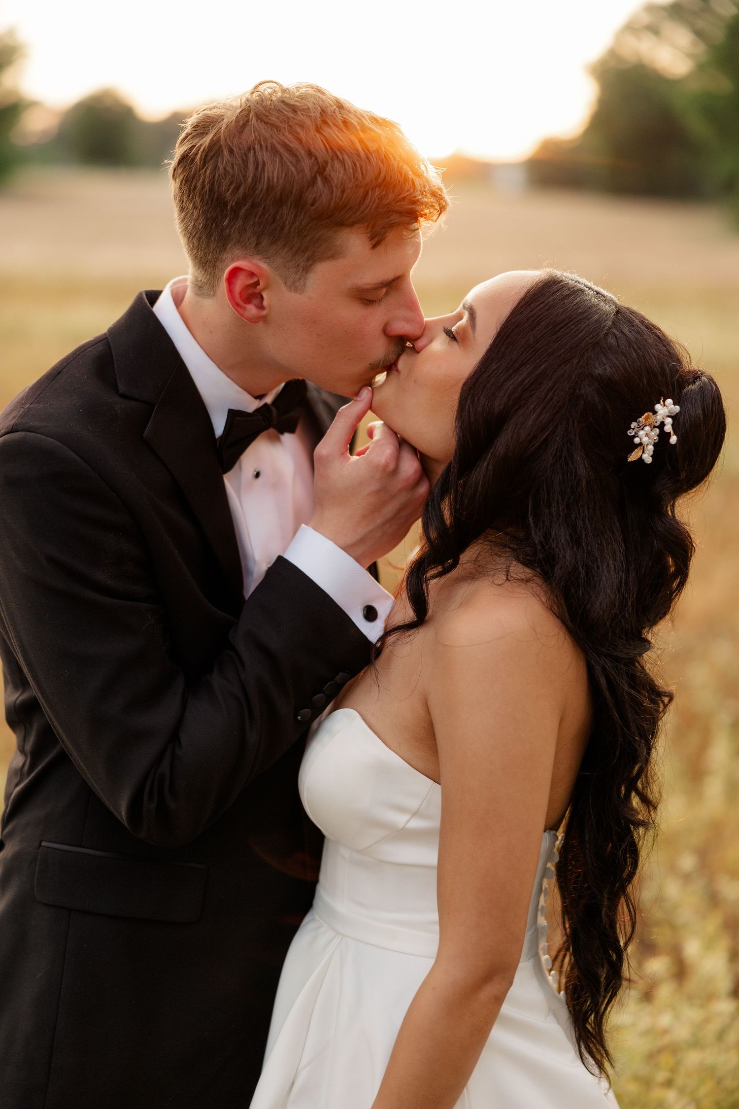 Romantic wedding couple sharing an intimate kiss during golden hour in a rural outdoor setting.