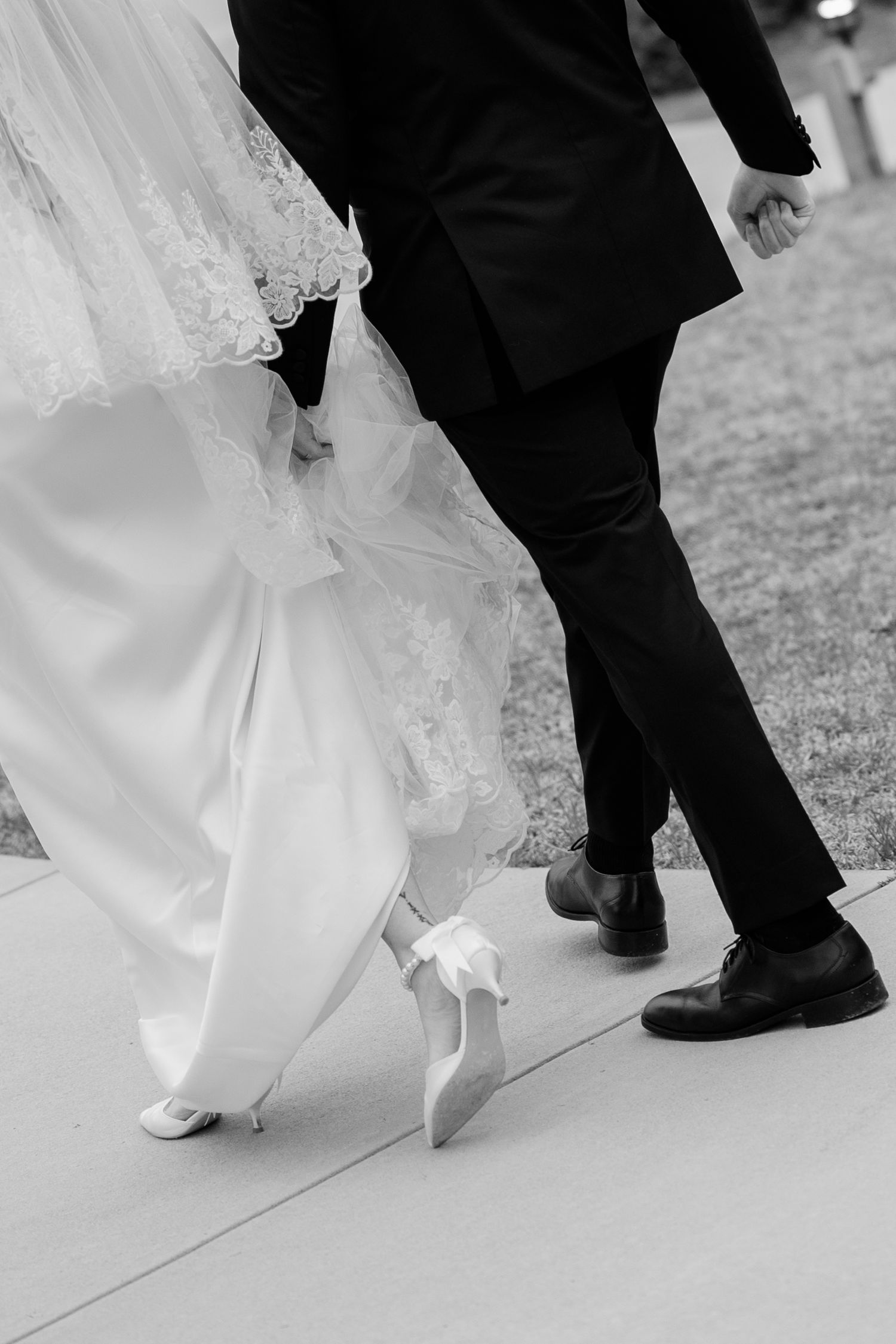 Black and white detail shot of couple walking showing dress hem and shoes.