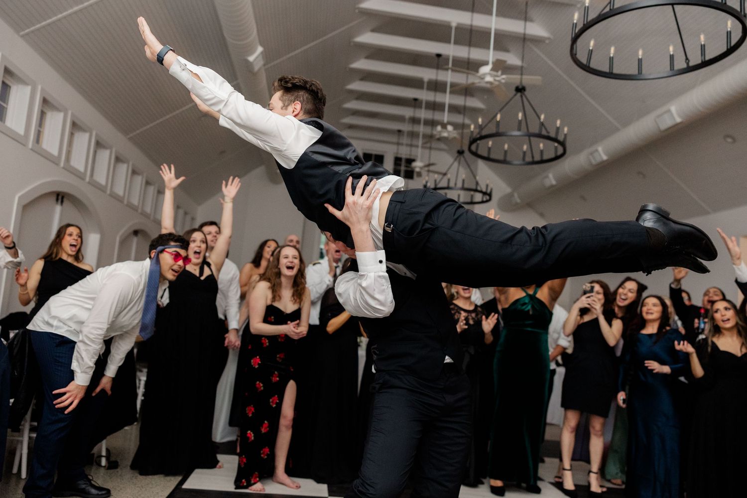Wedding guests dance and celebrate with energetic poses at an indoor reception.
