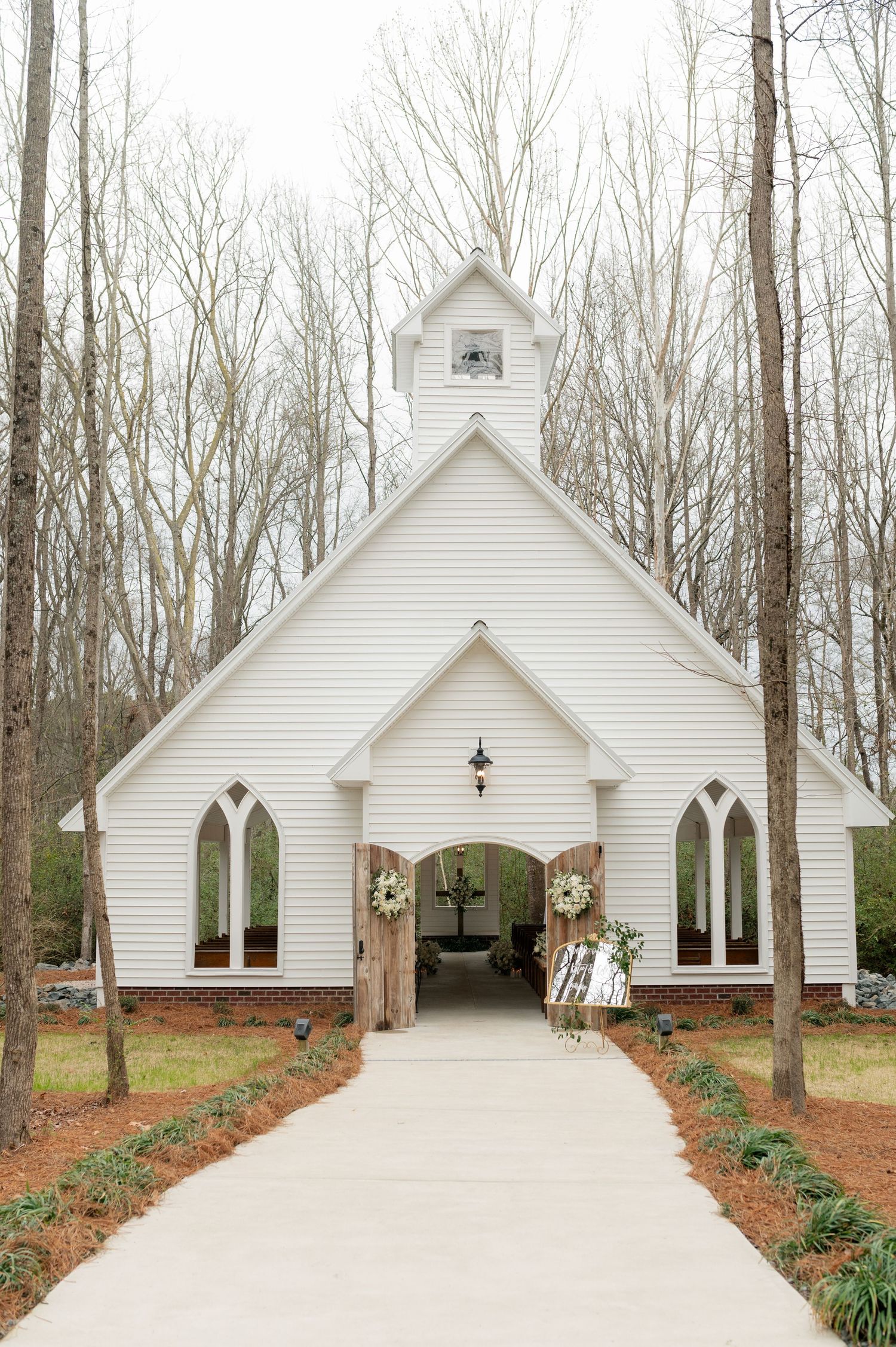 Charming white chapel with gothic windows surrounded by bare trees.