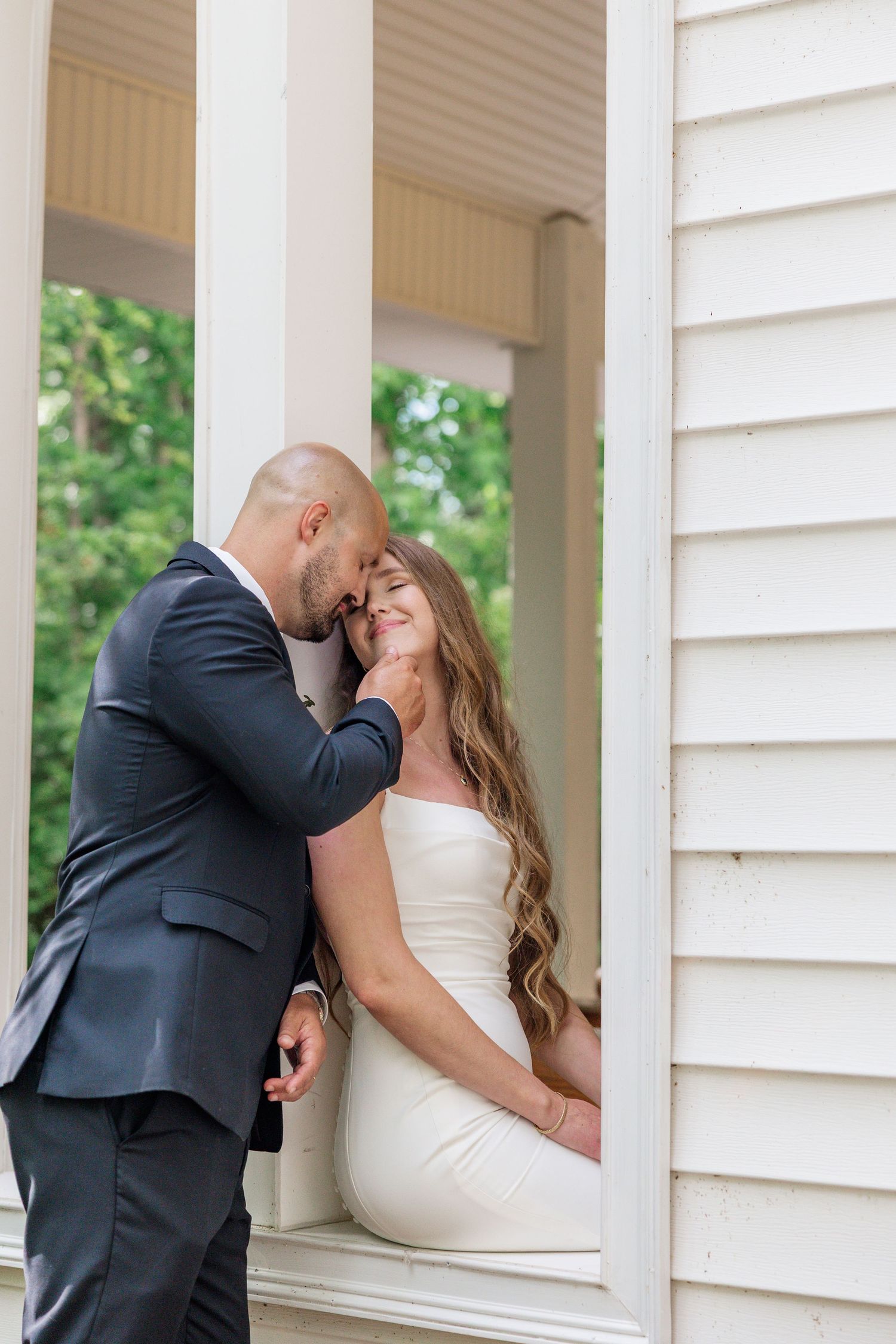 Romantic wedding couple shares intimate moments between white porch columns.