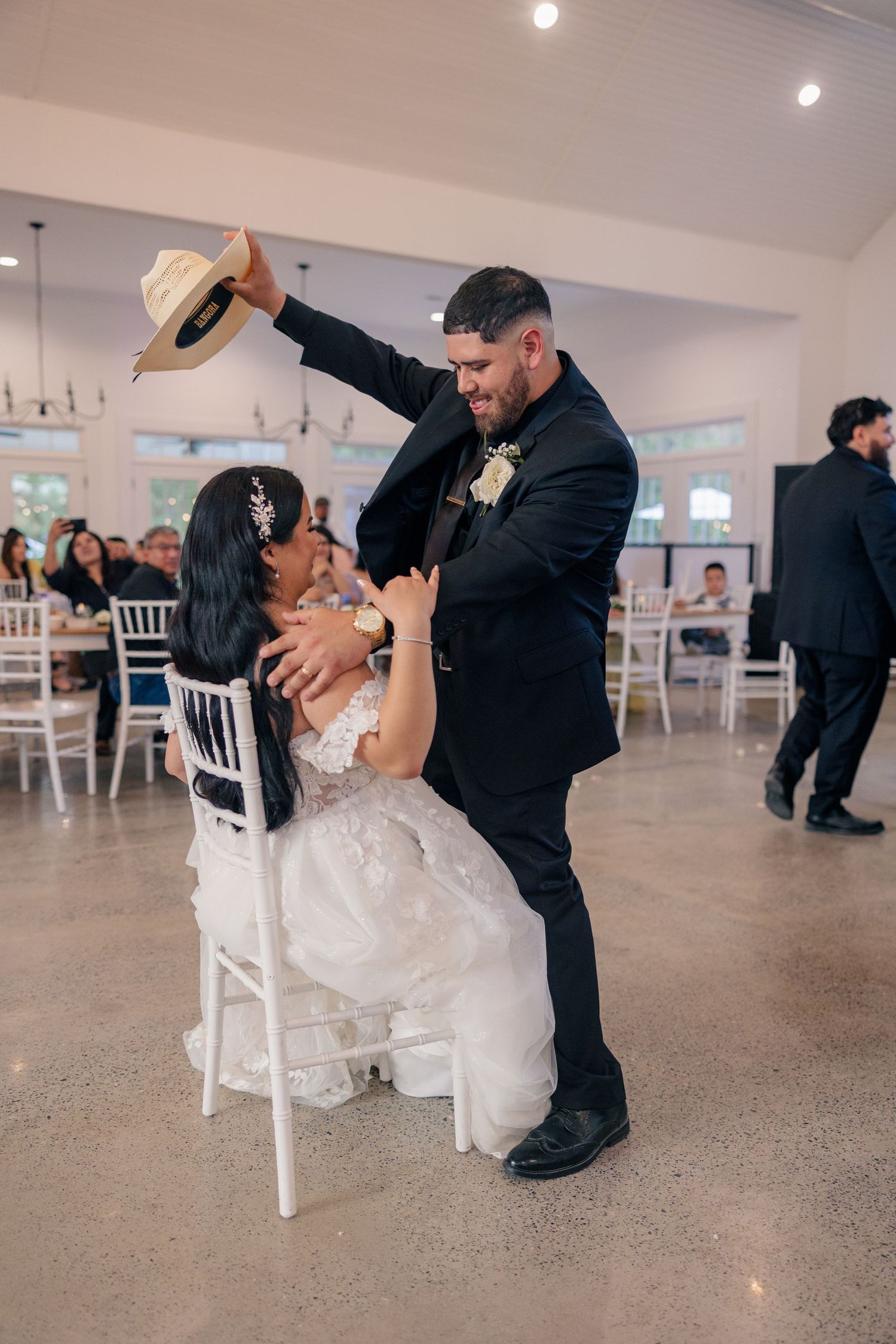 Newlyweds perform a playful dip dance sequence on white tile floor at their wedding reception.
