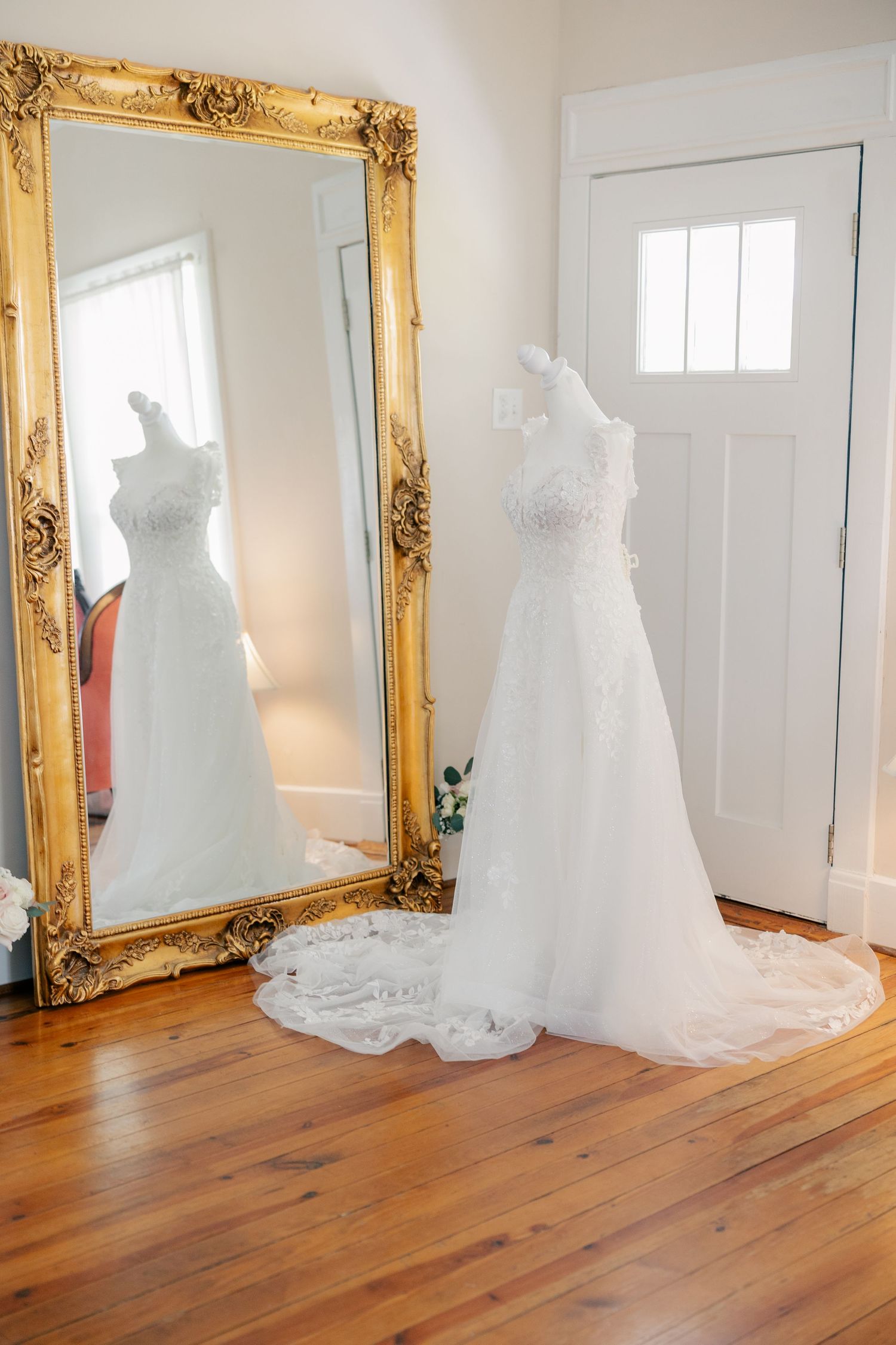 Wedding dresses on display in a bright room with ornate gold-framed mirrors and wooden flooring.