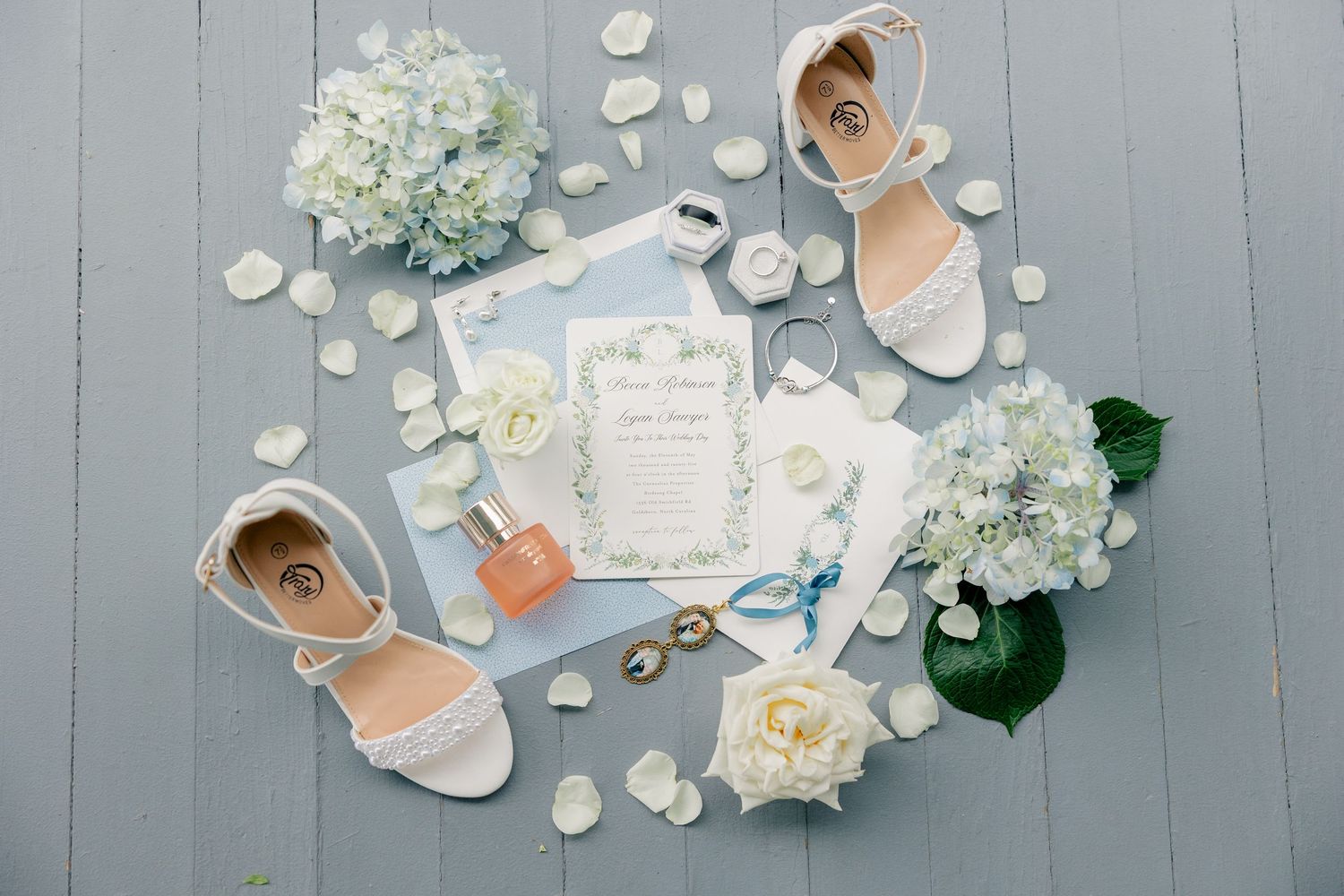 Wedding details including white hydrangeas, paper elements, wedding rings, and seashells arranged on a light gray surface.