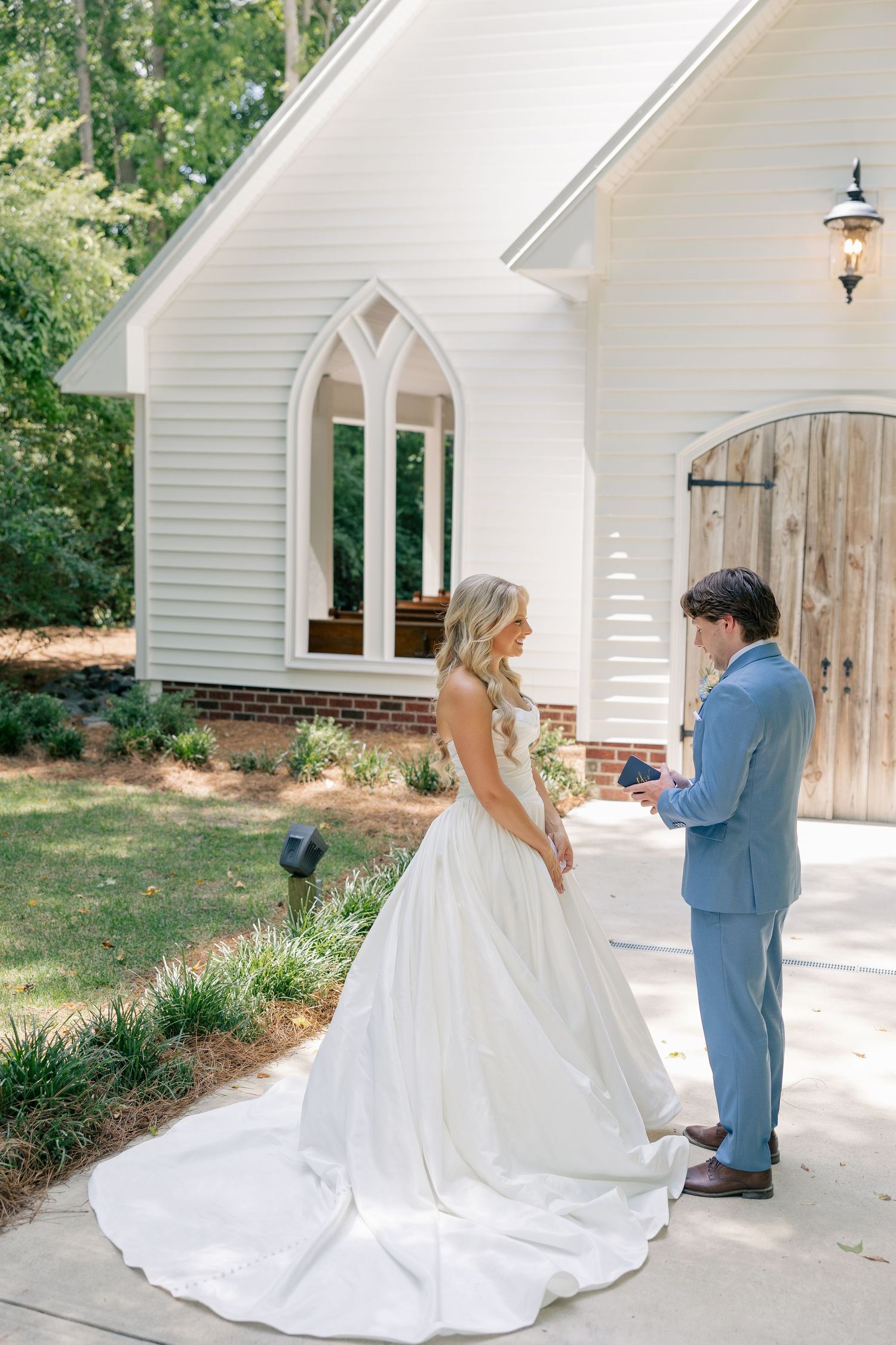 Groom reads vows to bride outside white chapel during first look.
