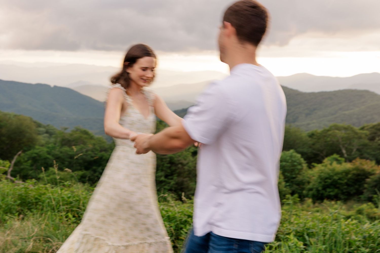 A couple dancing together in a scenic mountain landscape with green foliage and rolling hills in the background.