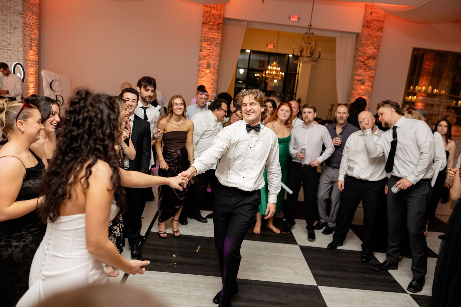 Wedding guests dance and celebrate on a black and white checkered dance floor at the reception.