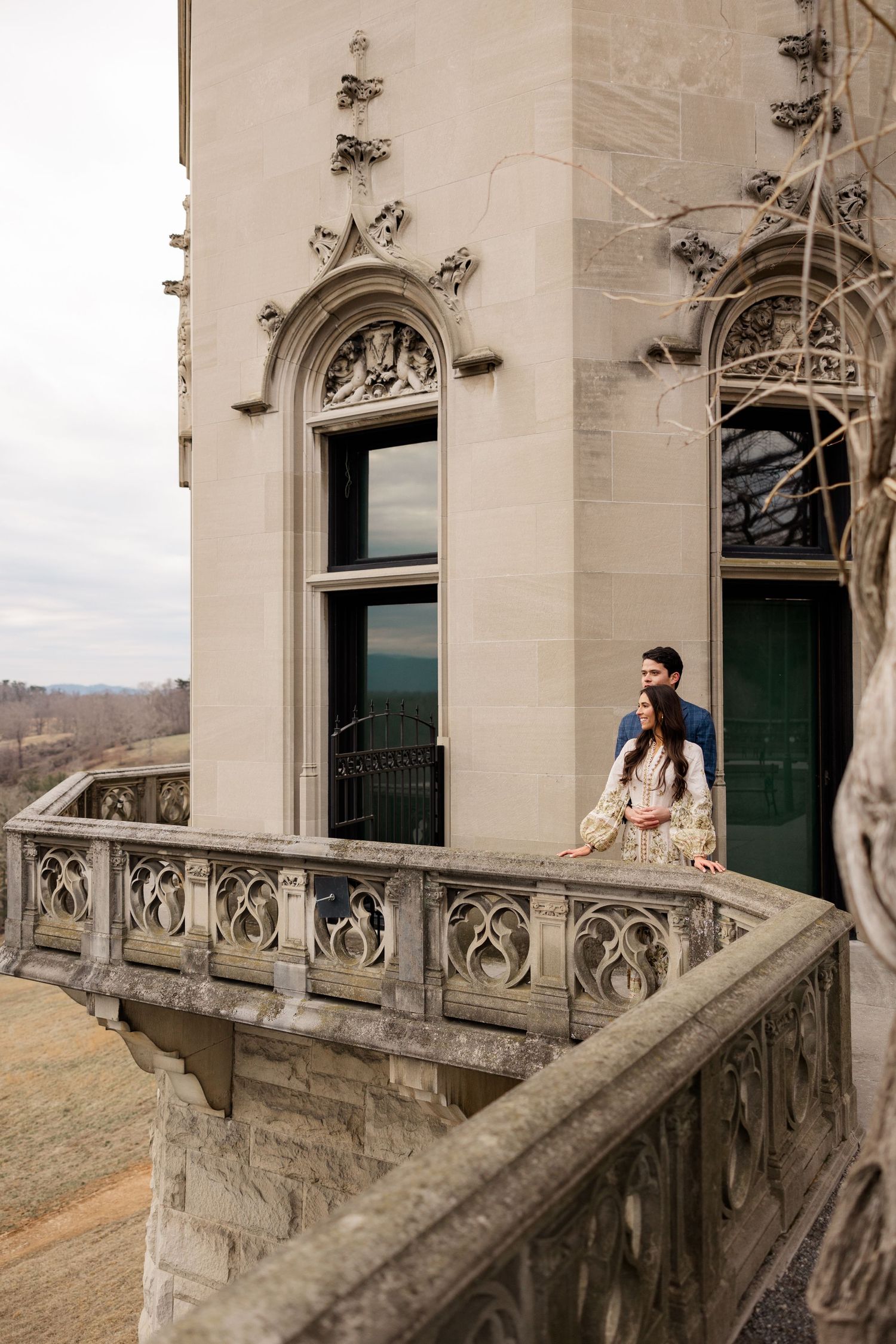Gothic stone balcony with ornate carvings on a historic castle overlooks a scenic mountain landscape.