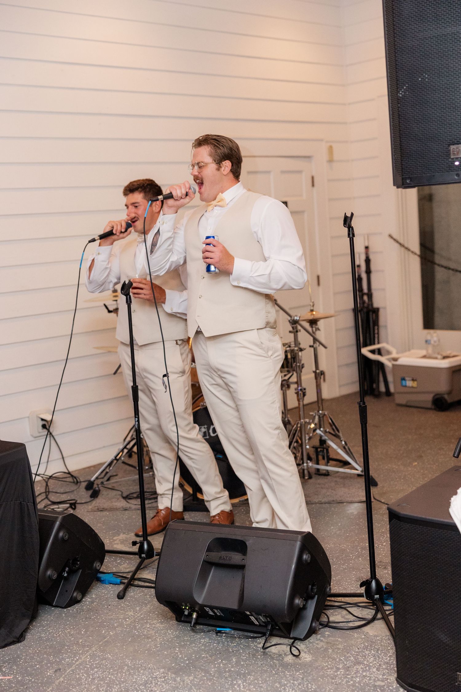 Two performers singing into microphones on stage at a wedding reception.