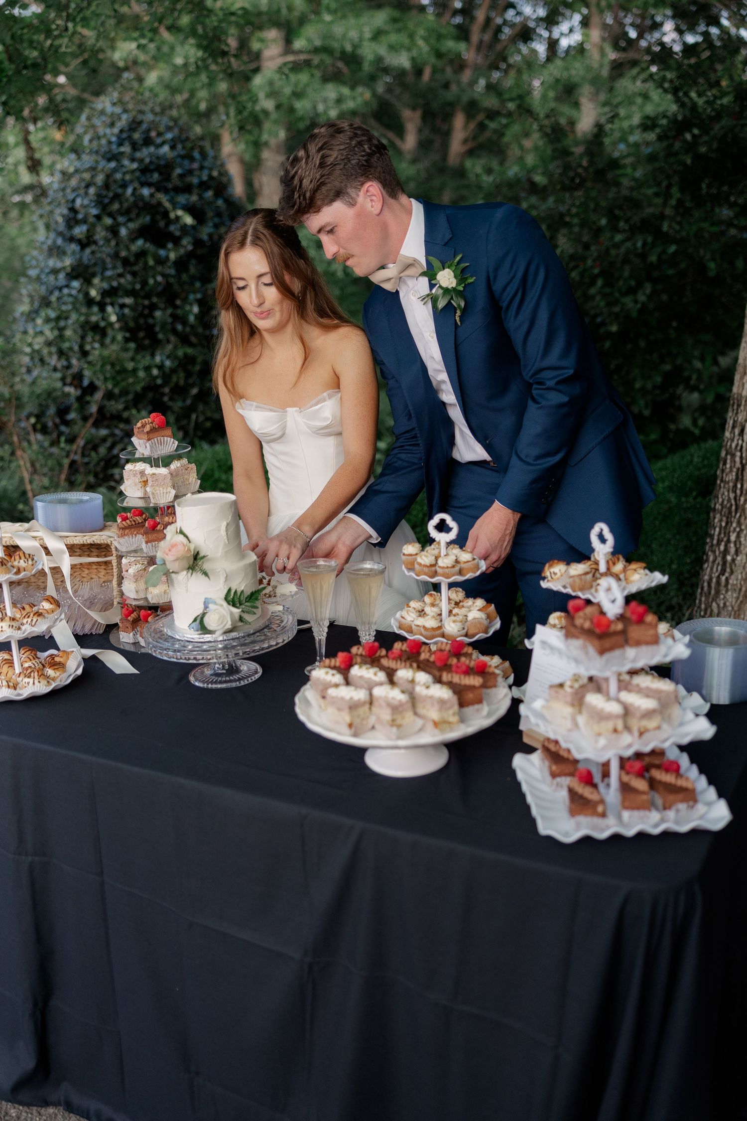 A wedding dessert table with tiered displays of cupcakes and treats on an elegant black tablecloth.