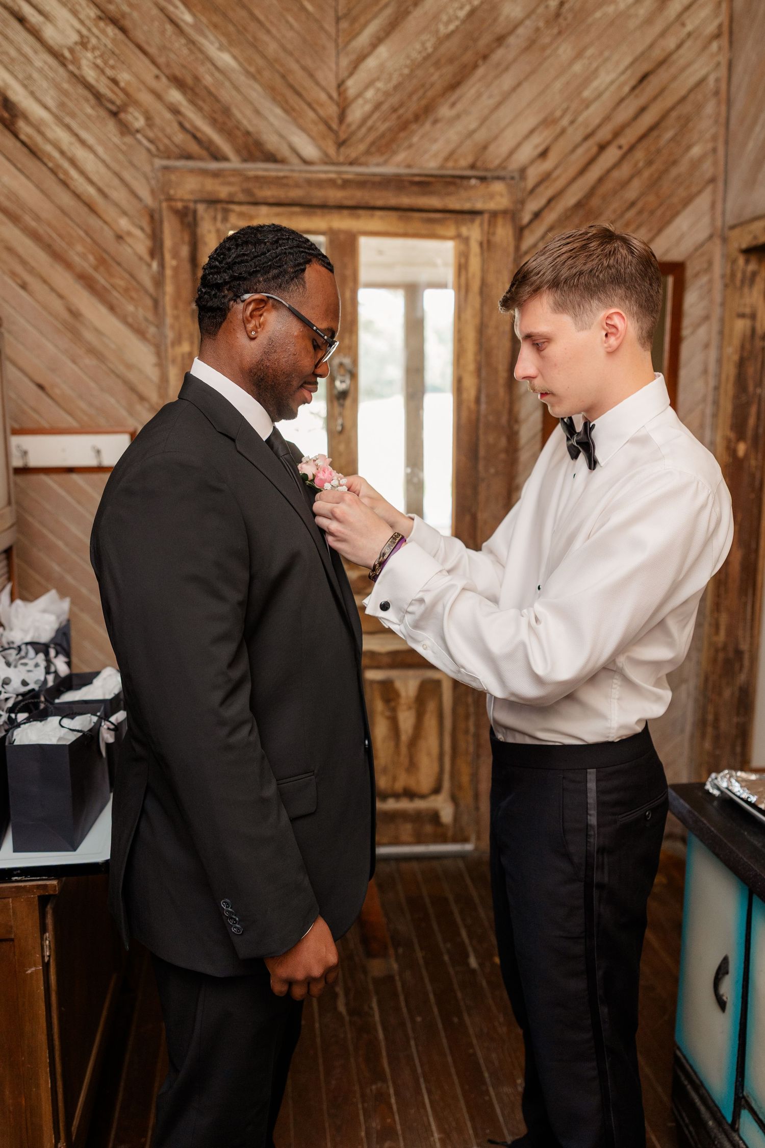 Men in formal attire getting dressed in a rustic wooden interior setting.