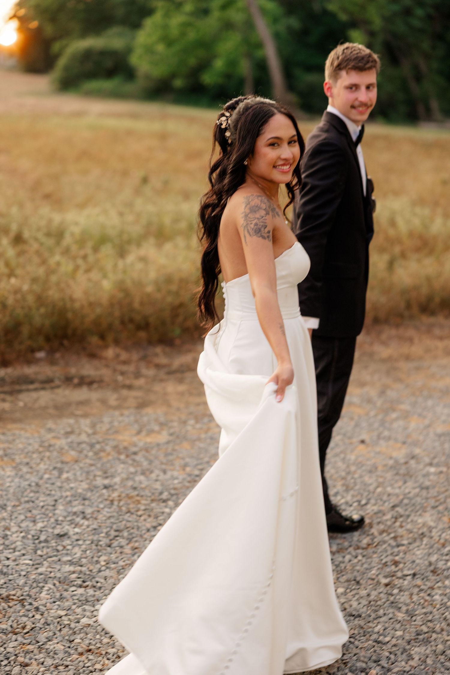 Bride in flowing white dress twirling and dancing outdoors at sunset.