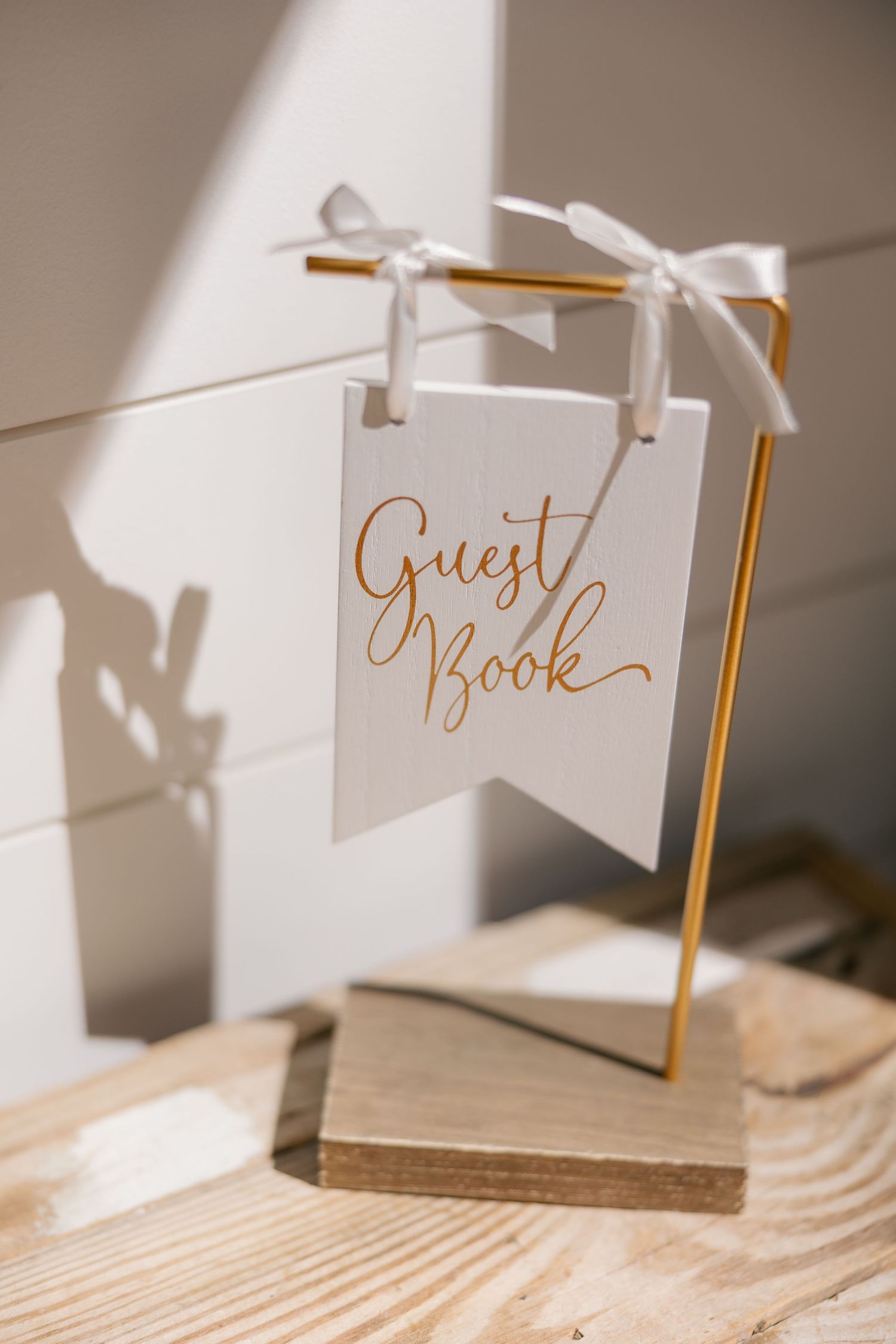 Elegant wedding guest book with gold trim and calligraphy text displays at place setting in soft natural light.