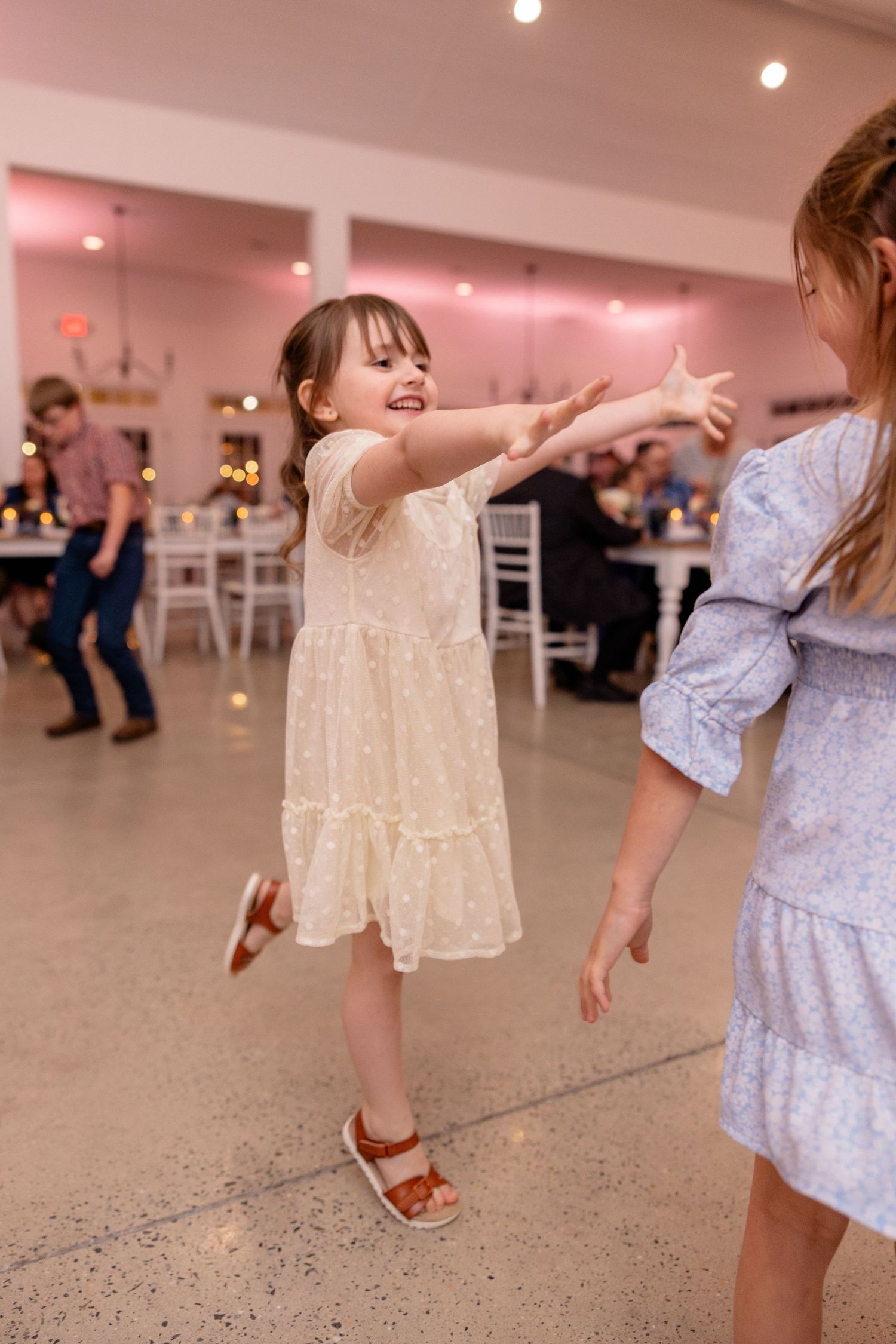 Children dancing and twirling in light dresses on the reception dance floor.